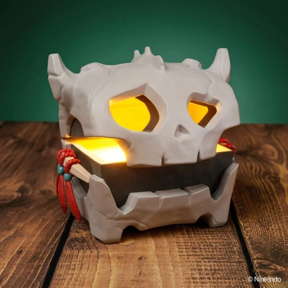 Un cofre gris con forma de calavera y luz amarilla brillante sobre una mesa de madera y fondo verde.