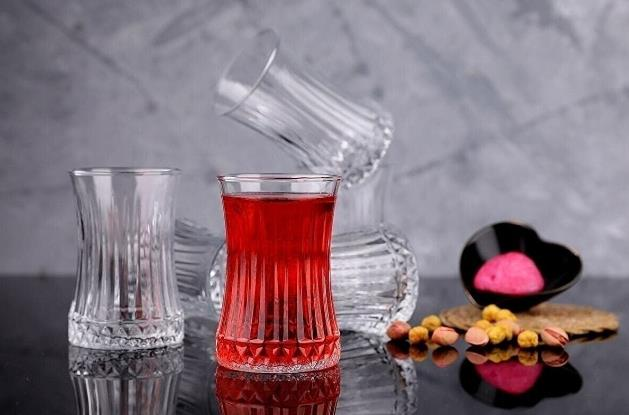 Koyu zemin üzerinde kırmızı çay bardağı, arkada diğer bardaklar ve kuruyemiş.