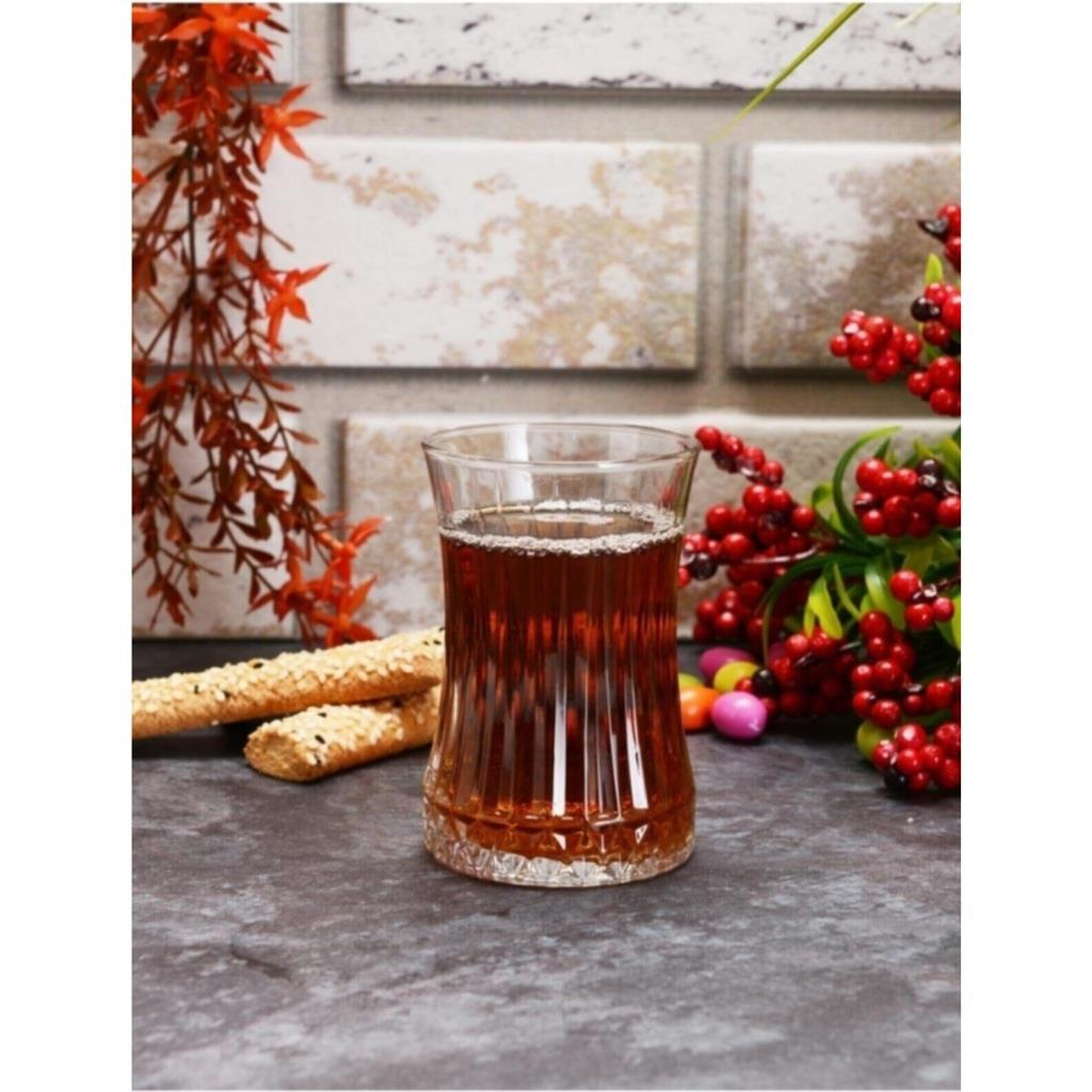 Koyu renkli bir zeminde, grissini ve kırmızı meyvelerle süslenmiş geleneksel ince belli bardakta çay.