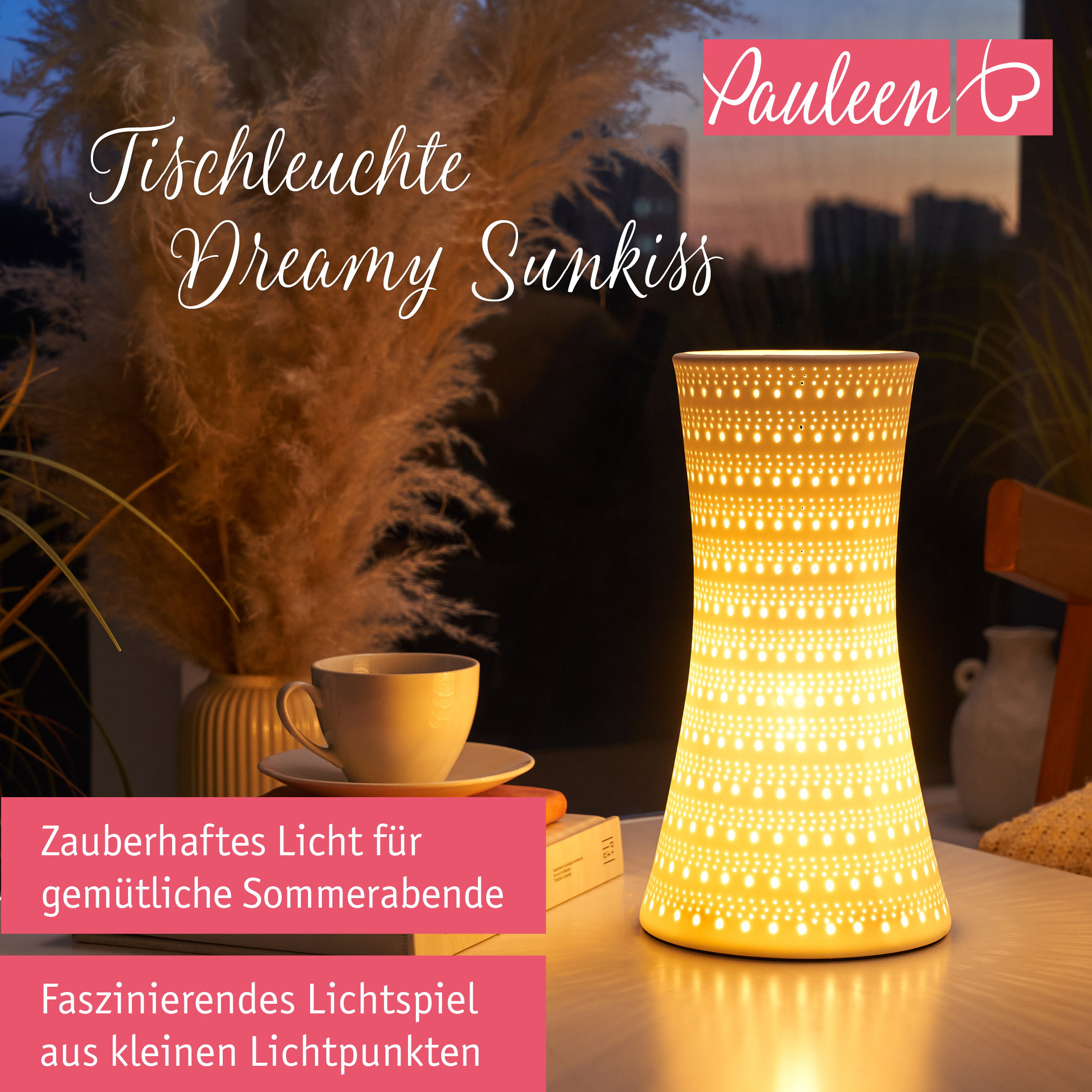 Eine beleuchtete weiße Tischlampe mit Punktmuster auf einem Tisch neben einer Tasse Kaffee und Blumen.