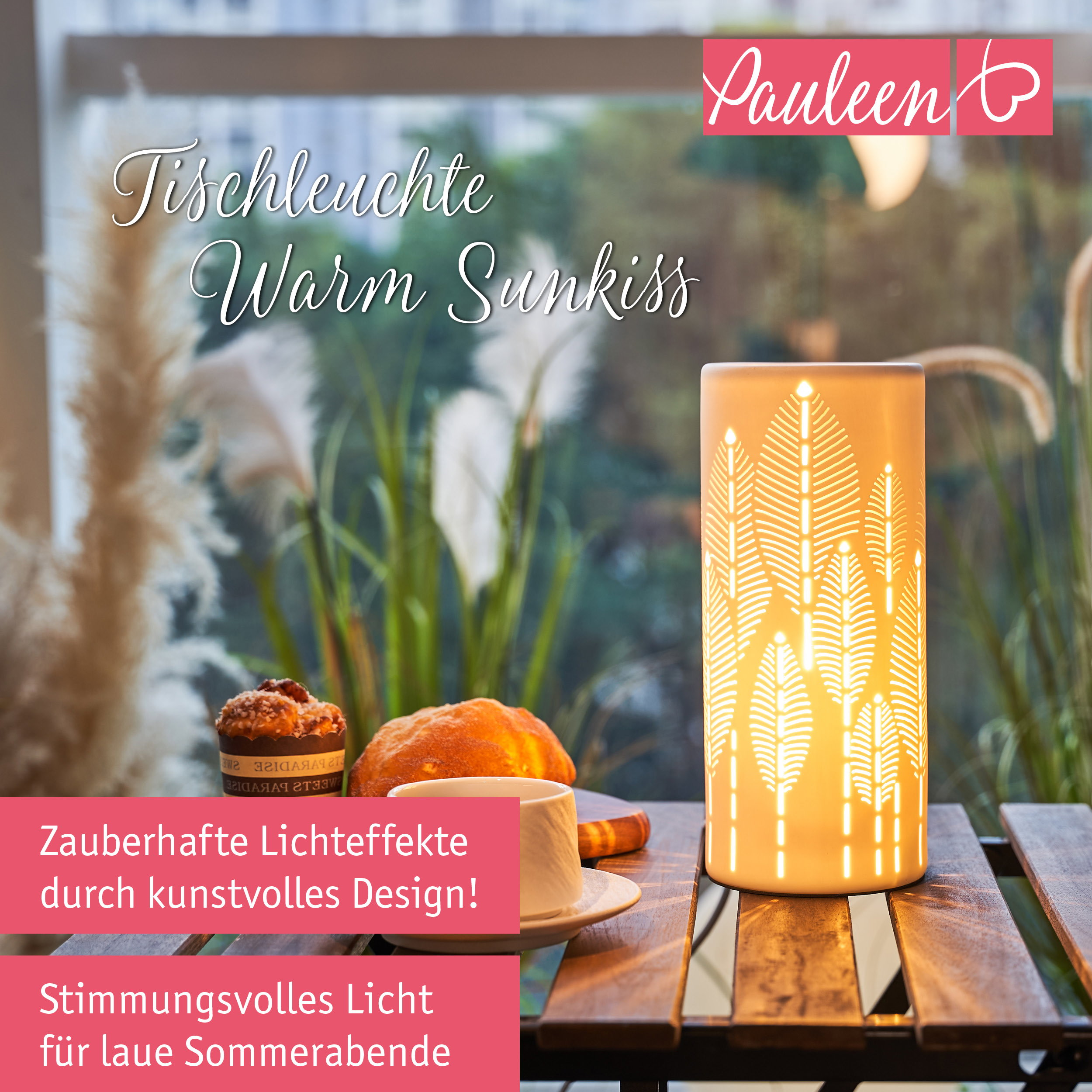 Eine beleuchtete Tischleuchte mit Blattmuster, eine Kaffeetasse und Gebäck auf einem Holztisch.