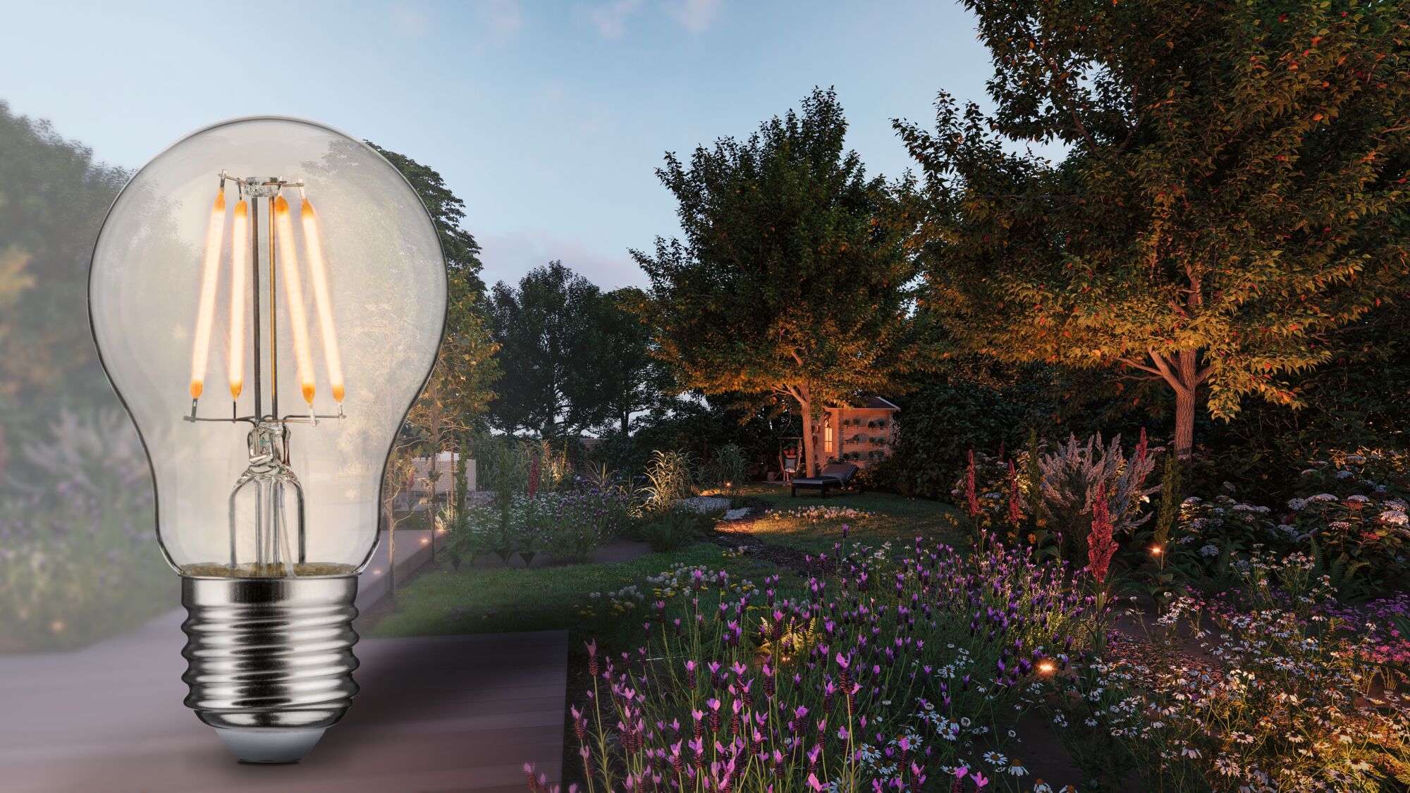 Una lampadina in primo piano contro un giardino illuminato con fiori e alberi al crepuscolo.