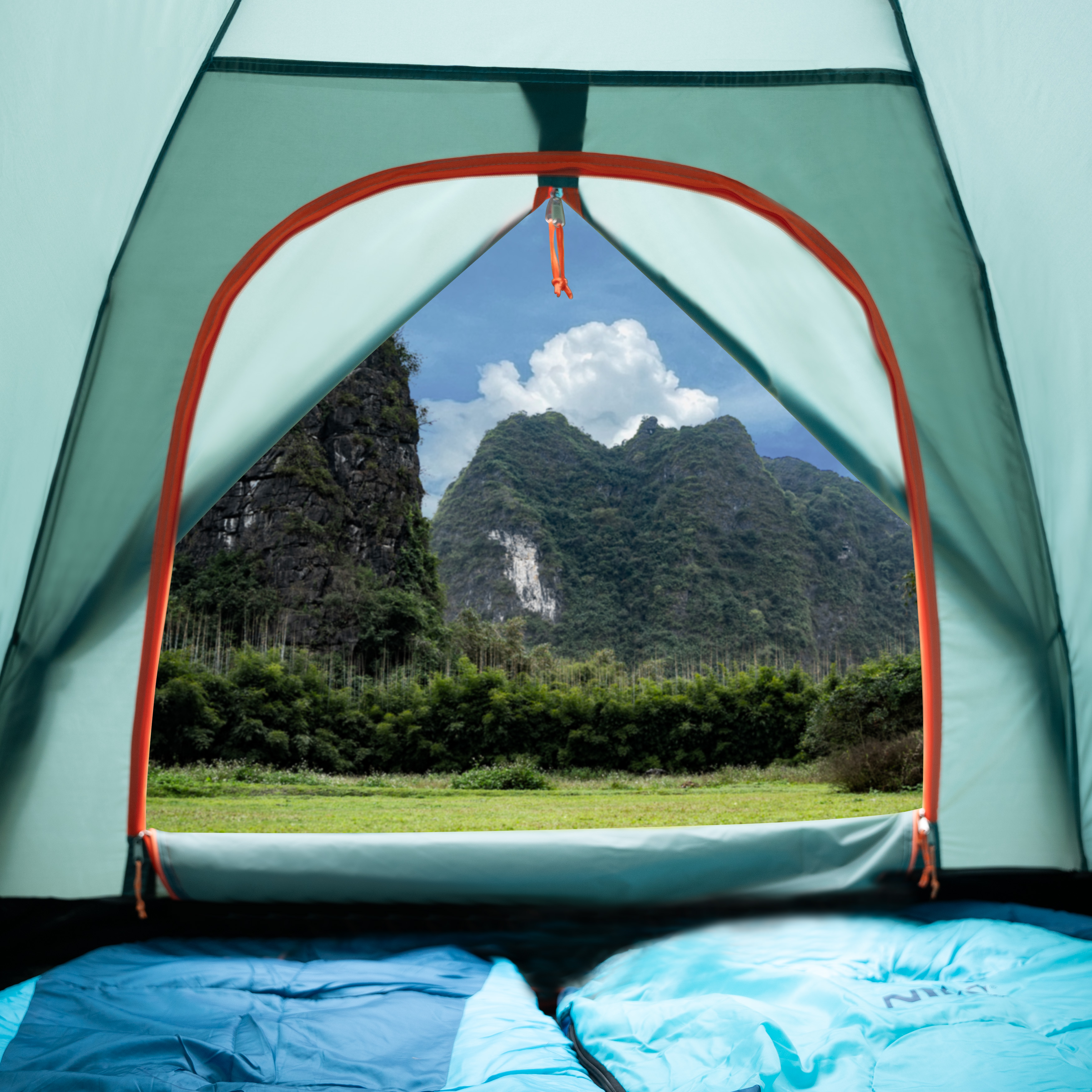 Vista desde el interior de una tienda con sacos de dormir azules hacia montañas verdes y cielo nublado.