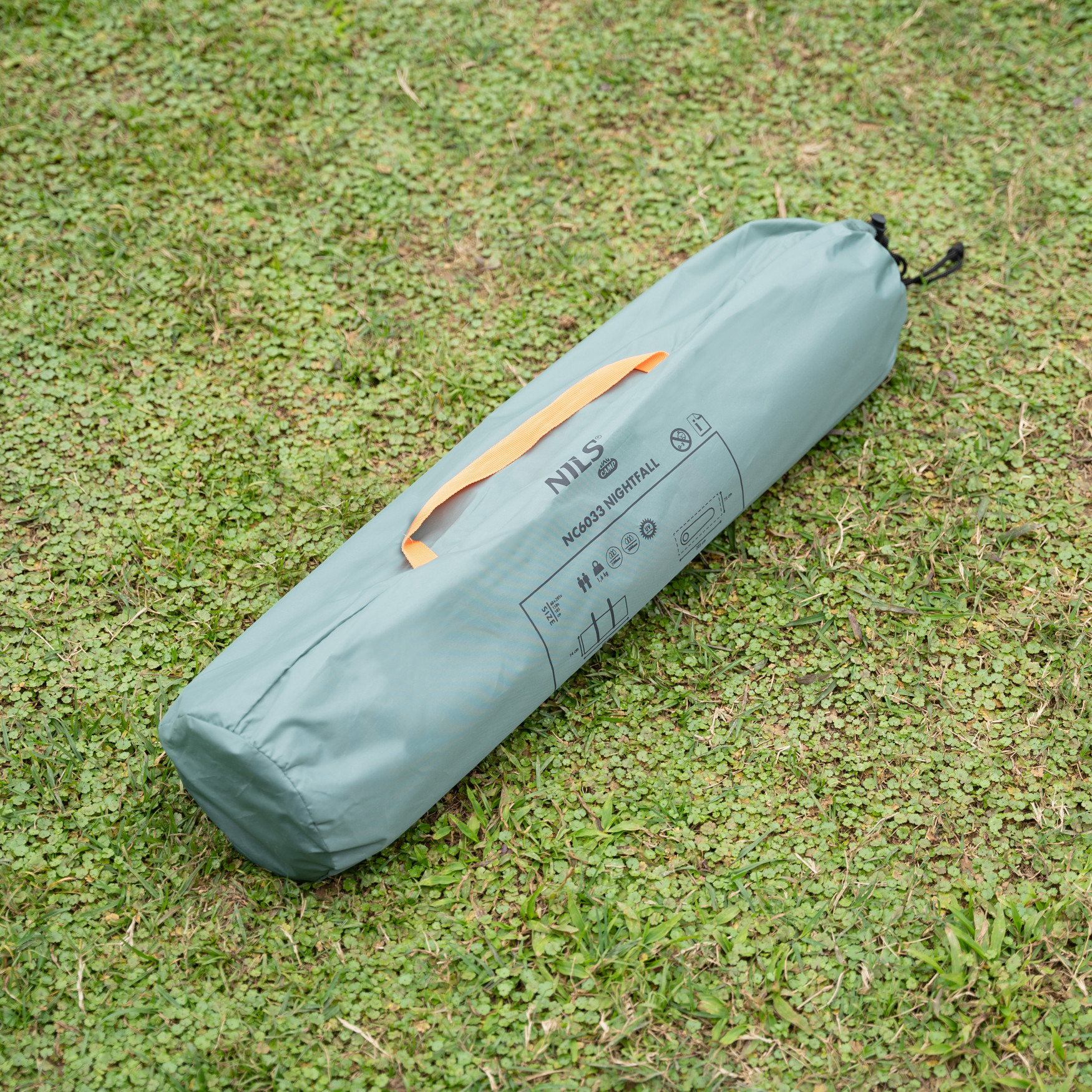 Una bolsa de tienda gris con asa naranja y cordón negro yace sobre un césped verde.