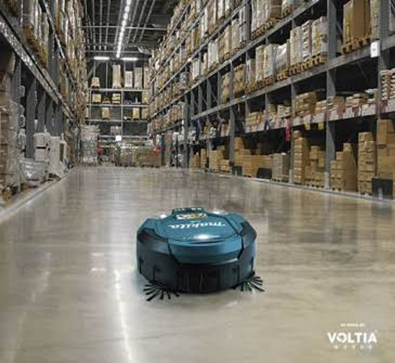 Un robot aspirapolvere blu pulisce il pavimento in cemento lucido di un grande magazzino con scaffali alti.