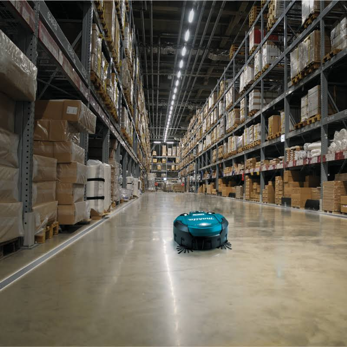 Un robot di pulizia autonomo verde acqua su un pavimento di magazzino lucido tra alte file di scaffali.