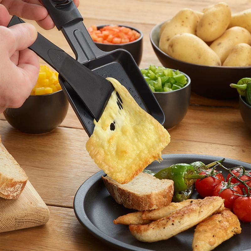 Geschmolzener Käse wird von einer Raclettepfanne auf Hähnchen und Brot gegeben.