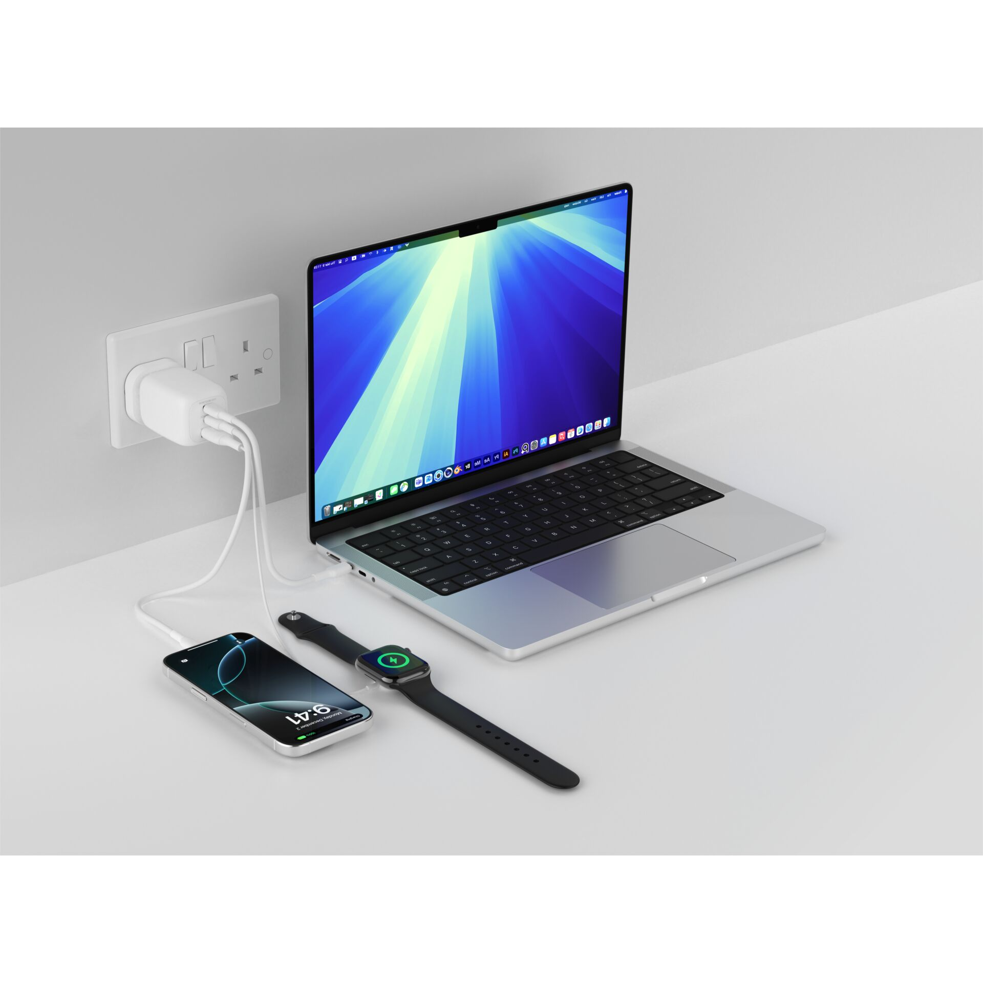 Un ordinateur portable, un téléphone et une montre connectée se chargent sur un bureau blanc.