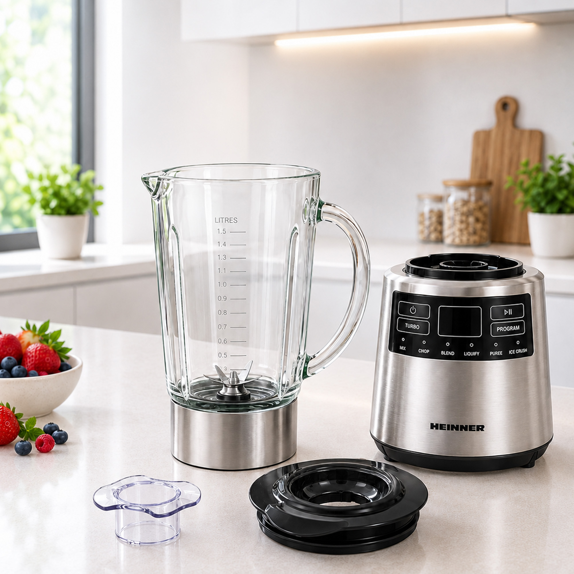 Un blender argenté Heinner avec cruche en verre, couvercle et petit insert sur un comptoir avec des baies.