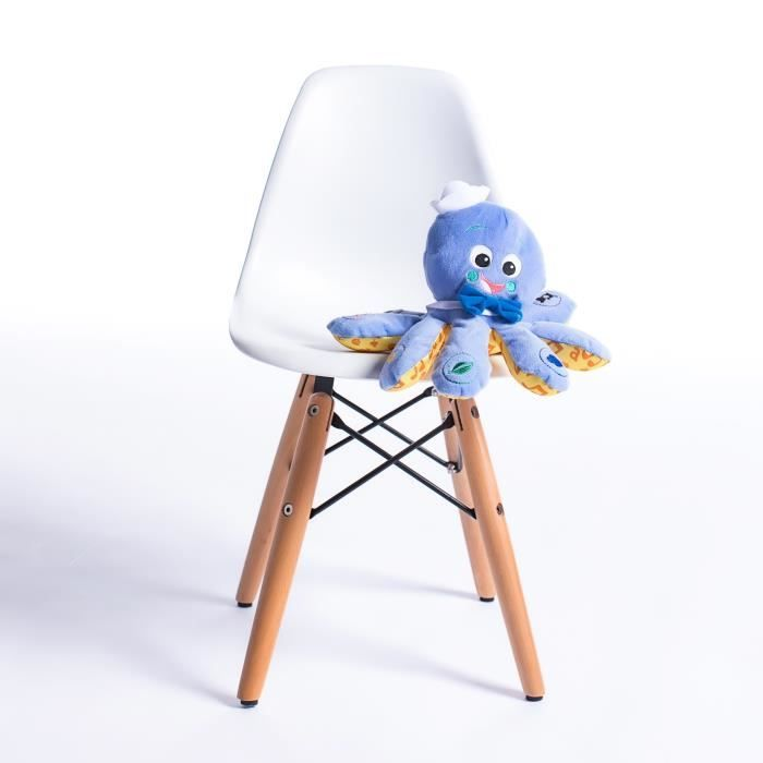 Un pulpo de peluche azul con gorra y pajarita sentado en una silla blanca con patas de madera sobre fondo blanco.