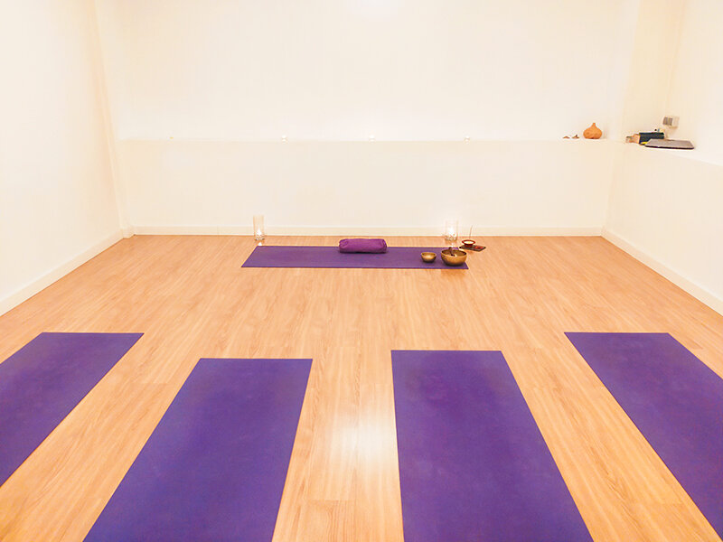 Estudio de yoga con suelo de madera, esterillas moradas y cuencos.