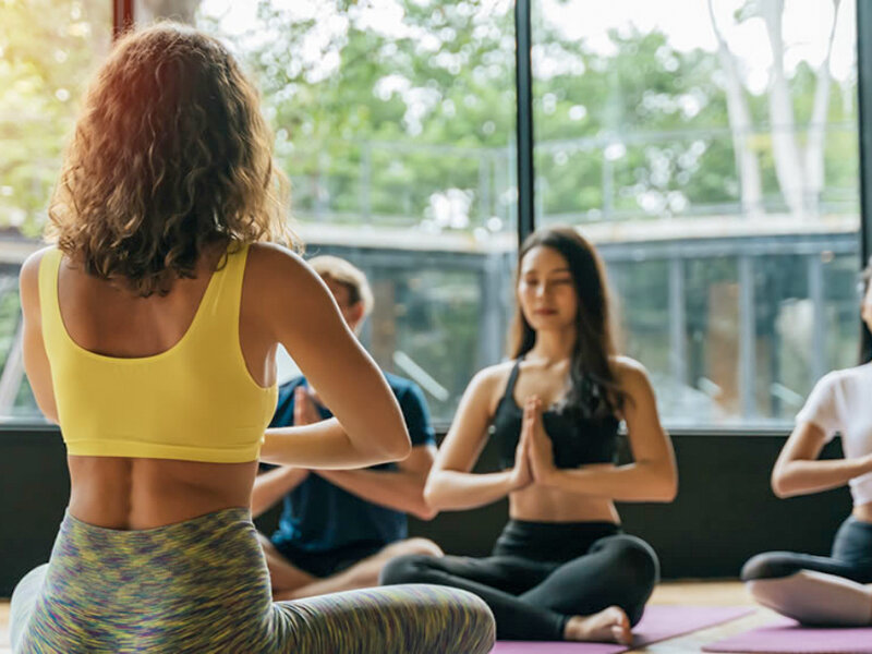 Un grupo diverso de personas sentado con las piernas cruzadas en esterillas de yoga en un estudio luminoso, meditando.