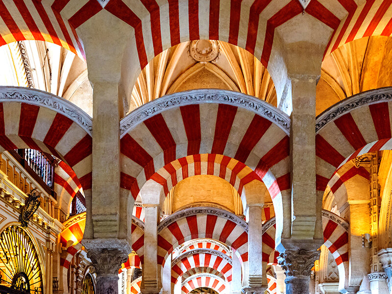 Arcos de herradura rojos y blancos y columnas moriscas dentro de un edificio histórico.