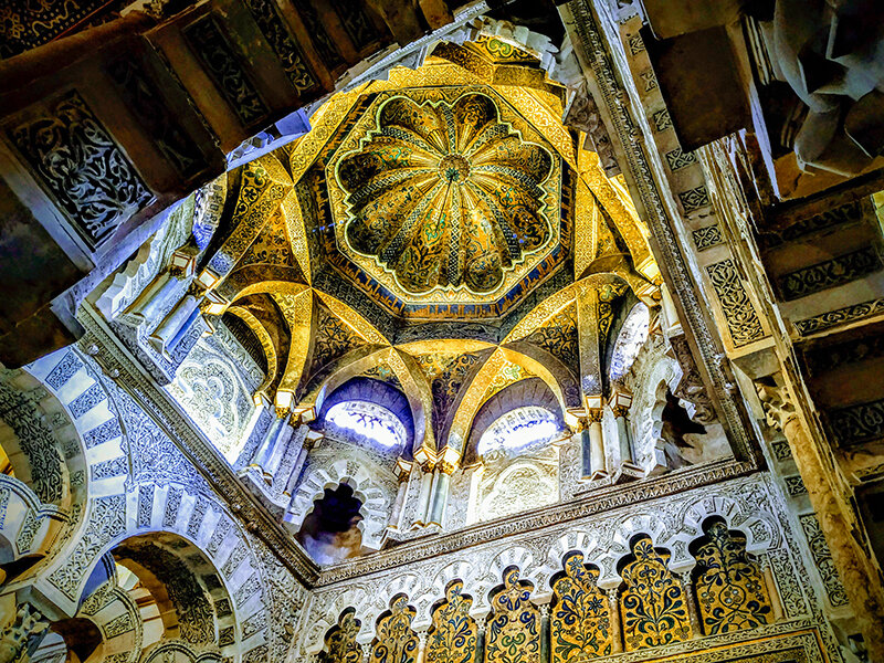 Cúpula dorada ornamentada y arcos moriscos en una vista interior.