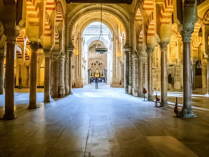 Gran sala histórica con hileras de columnas y arcos de rayas rojas y blancas, una persona de pie a lo lejos.