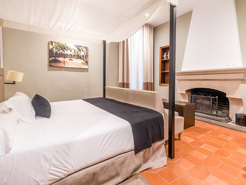 Acogedor dormitorio con cama con dosel, chimenea y suelos de baldosas de terracota.