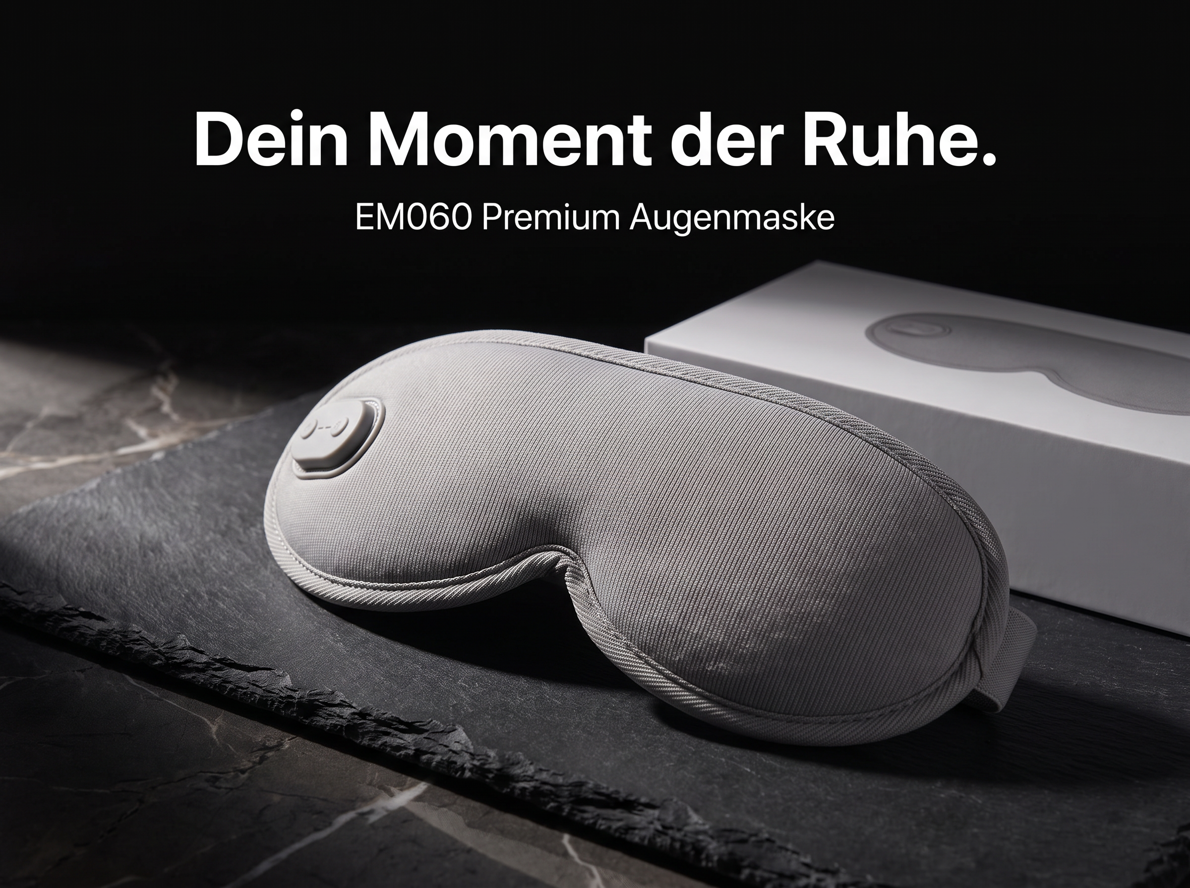 Eine graue EM060 Premium Augenmaske liegt auf einer dunklen Schieferplatte vor einer weißen Verpackung.