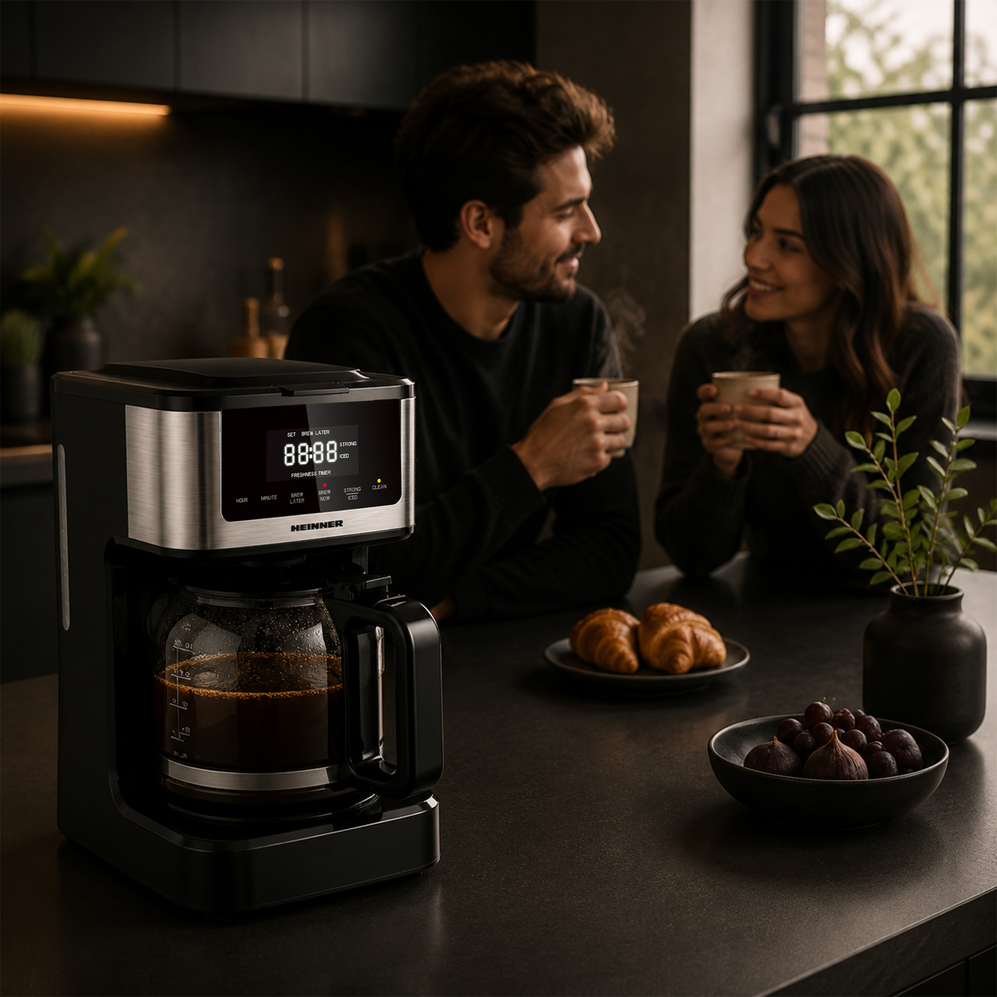Een koffiezetapparaat staat op het aanrecht terwijl een koppel koffie drinkt op de achtergrond.