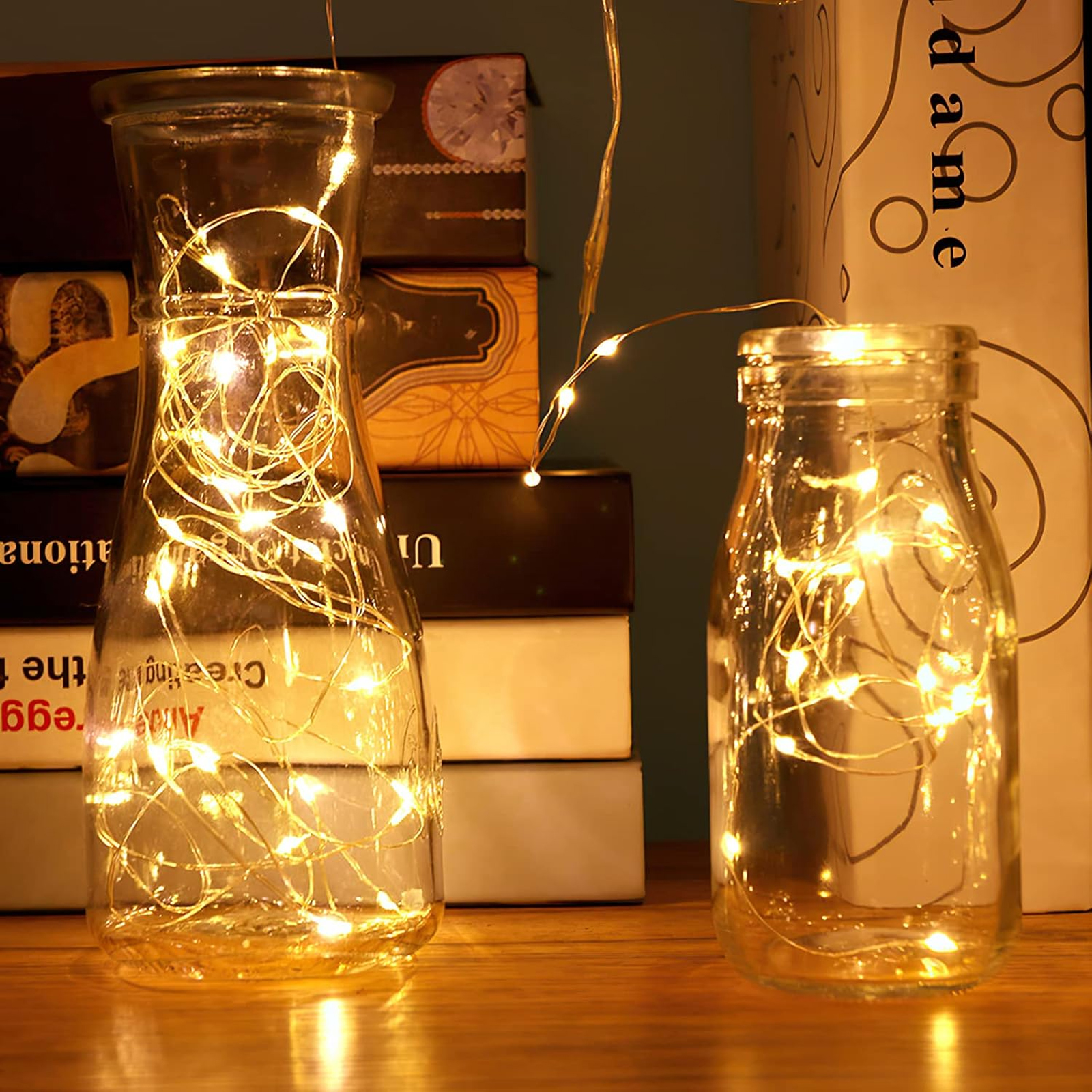 Zwei Glastöpfe mit Lichterketten stehen auf einem Holzbrett vor stapelten Büchern.