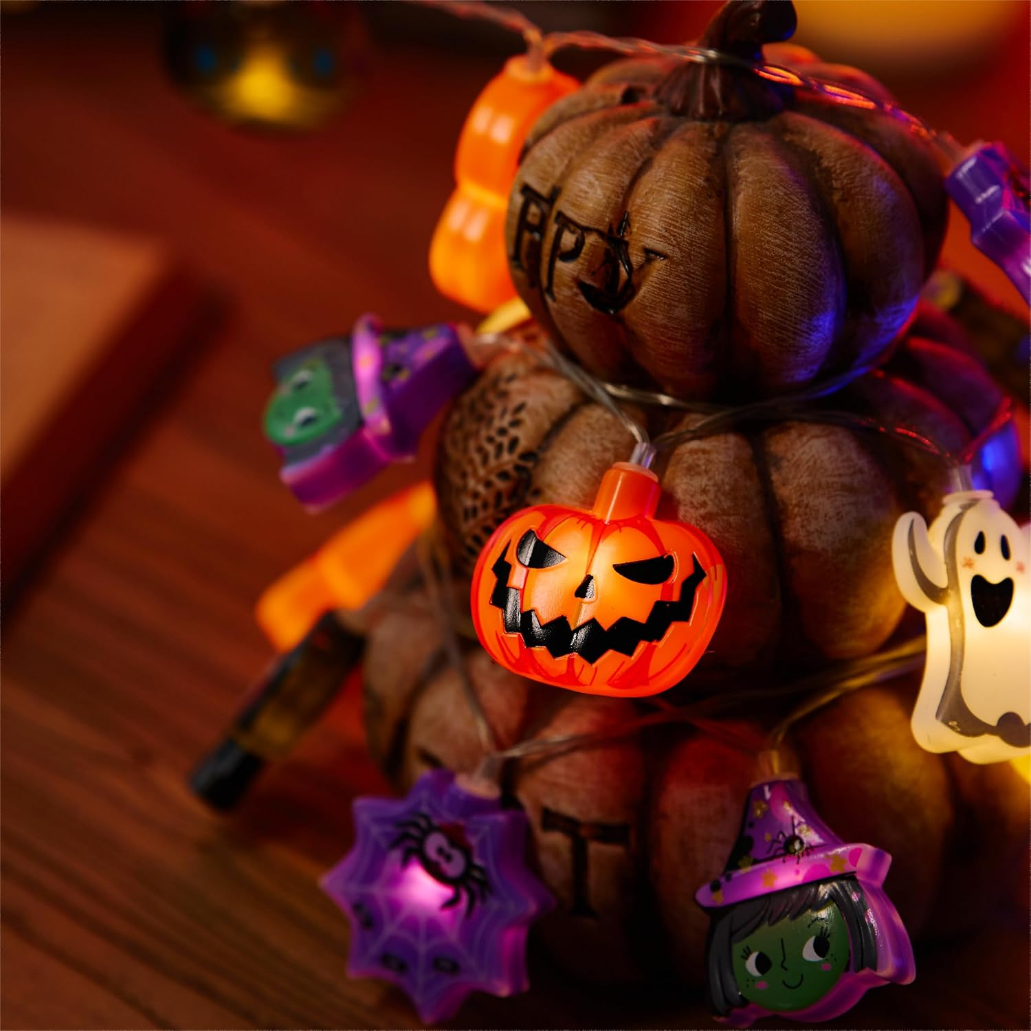 Stapel aus dekorierten Kürbissen mit bunter Halloween-Lichterkette auf einem Holztisch.