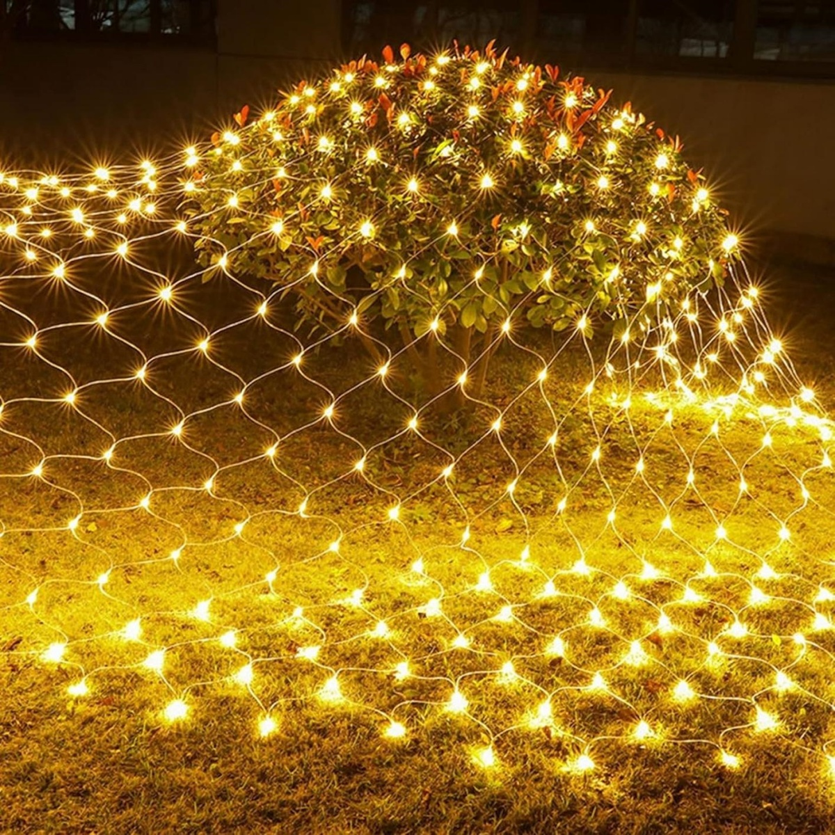 Ein Busch im Garten ist nachts mit einem Netz aus gelben Lichterketten bedeckt.
