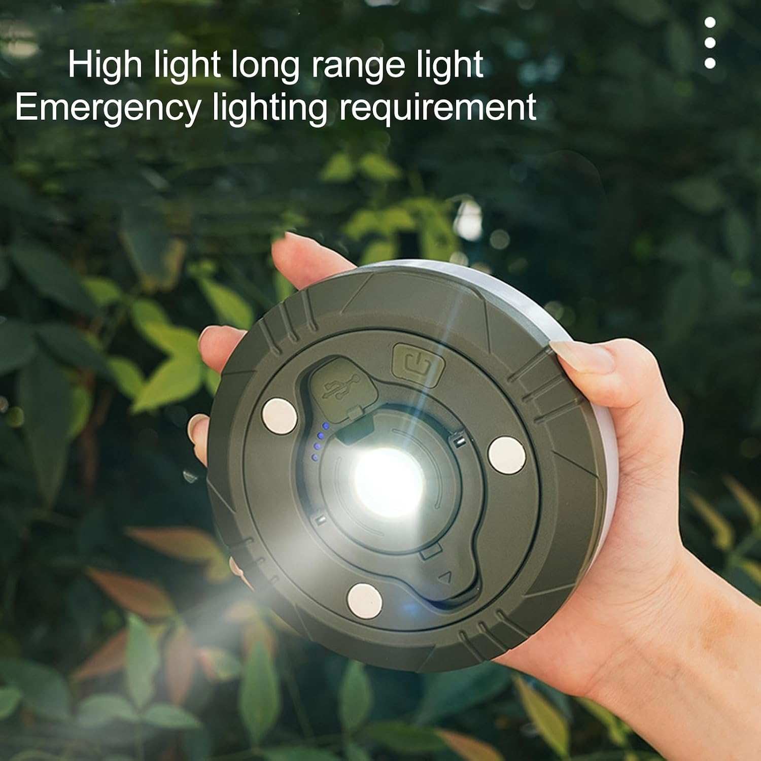 Eine Hand hält eine runde, olivgrüne LED-Notlampe mit beleuchteter Mitte und Text im Hintergrund.