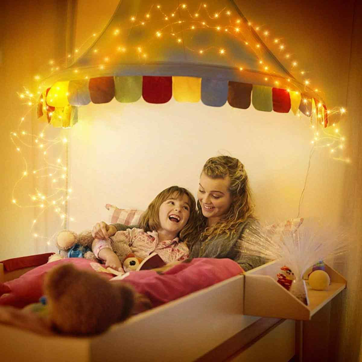 Eine Frau und ein Kind lachen unter einem beleuchteten Himmelbett mit bunten Flaggen und Lichterketten.