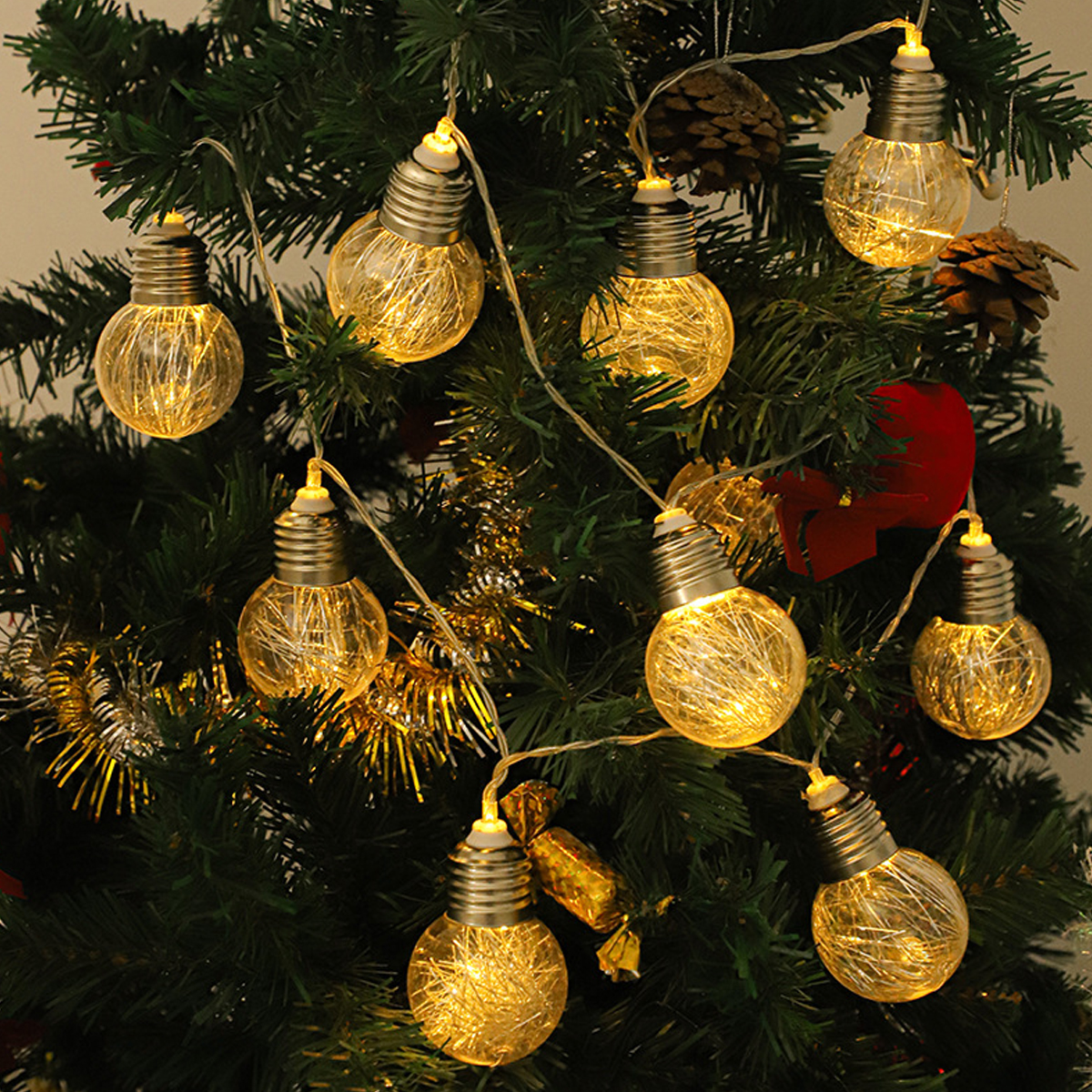 Warm leuchtende lichterketten in Glühbirnenform hängen an einem grünen Tannenbaum.
