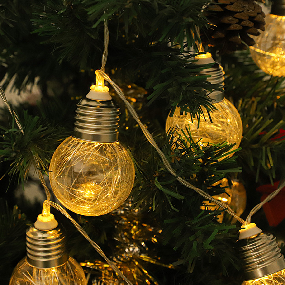 Glühende Lichterketten in Glühbirnenform hängen an einem Weihnachtsbaum mit Tannenzapfen.
