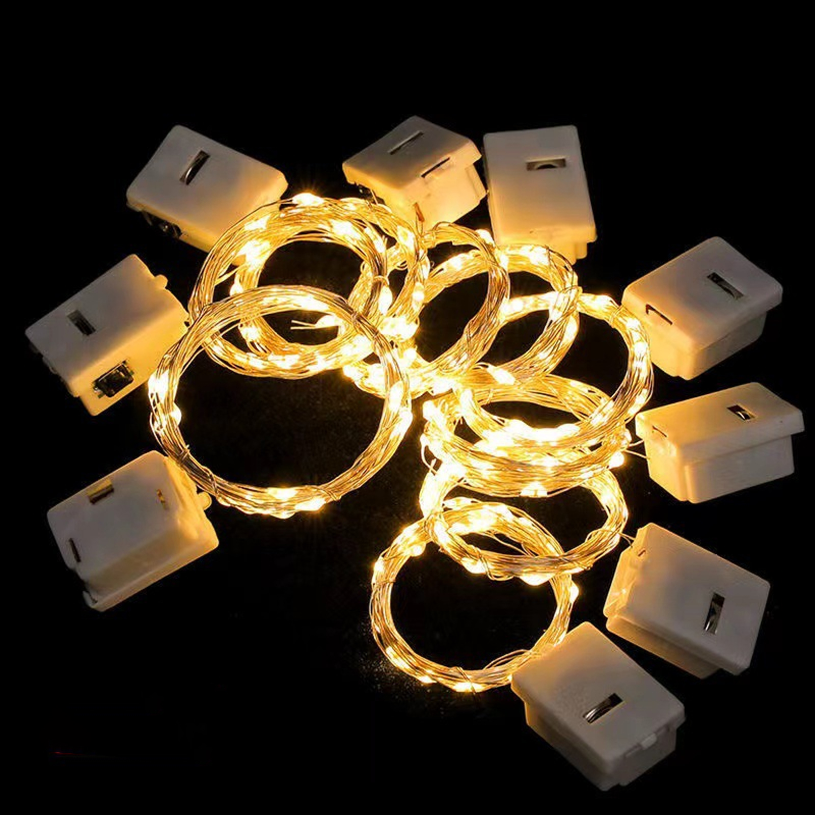 Mehrere helle, gewickelte Lichterketten mit kleinen weißen Batterieboxen auf schwarzem Hintergrund.