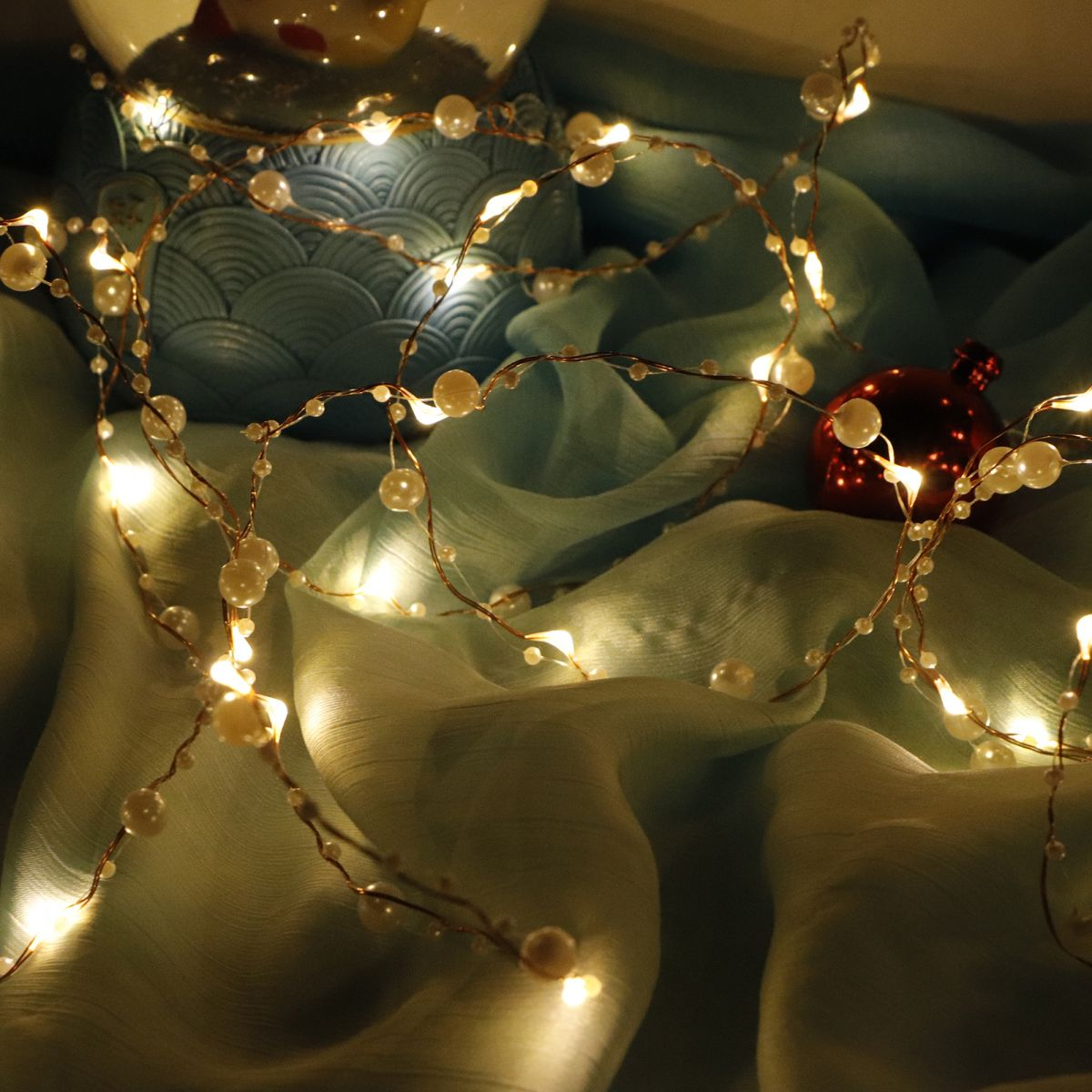 Lichterkette und Perlen auf blauem Stoff mit roter Kugel.