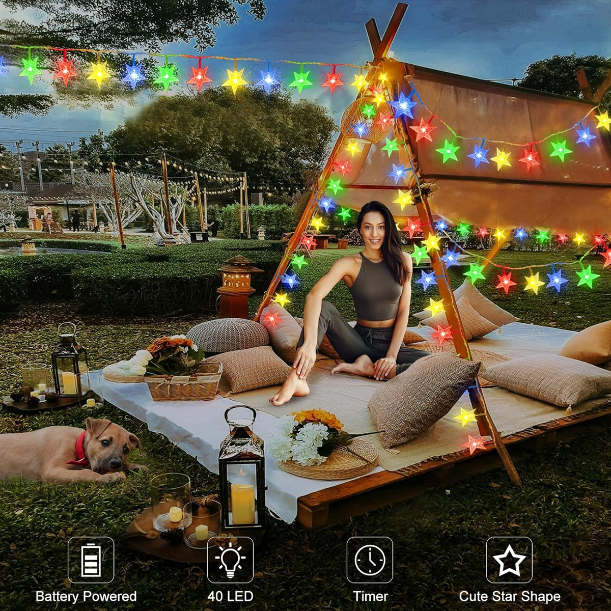 Eine lächelnde Frau sitzt in einem Zelt mit bunten Sternen-Lichterketten; ein Hund liegt auf dem Rasen.