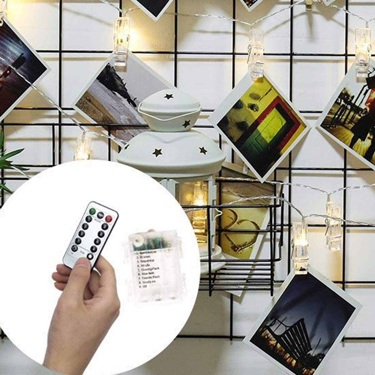 Eine Hand hält eine Fernbedienung vor einer weißen Laterne und Lichterketten mit Fotos an einem Gitter.