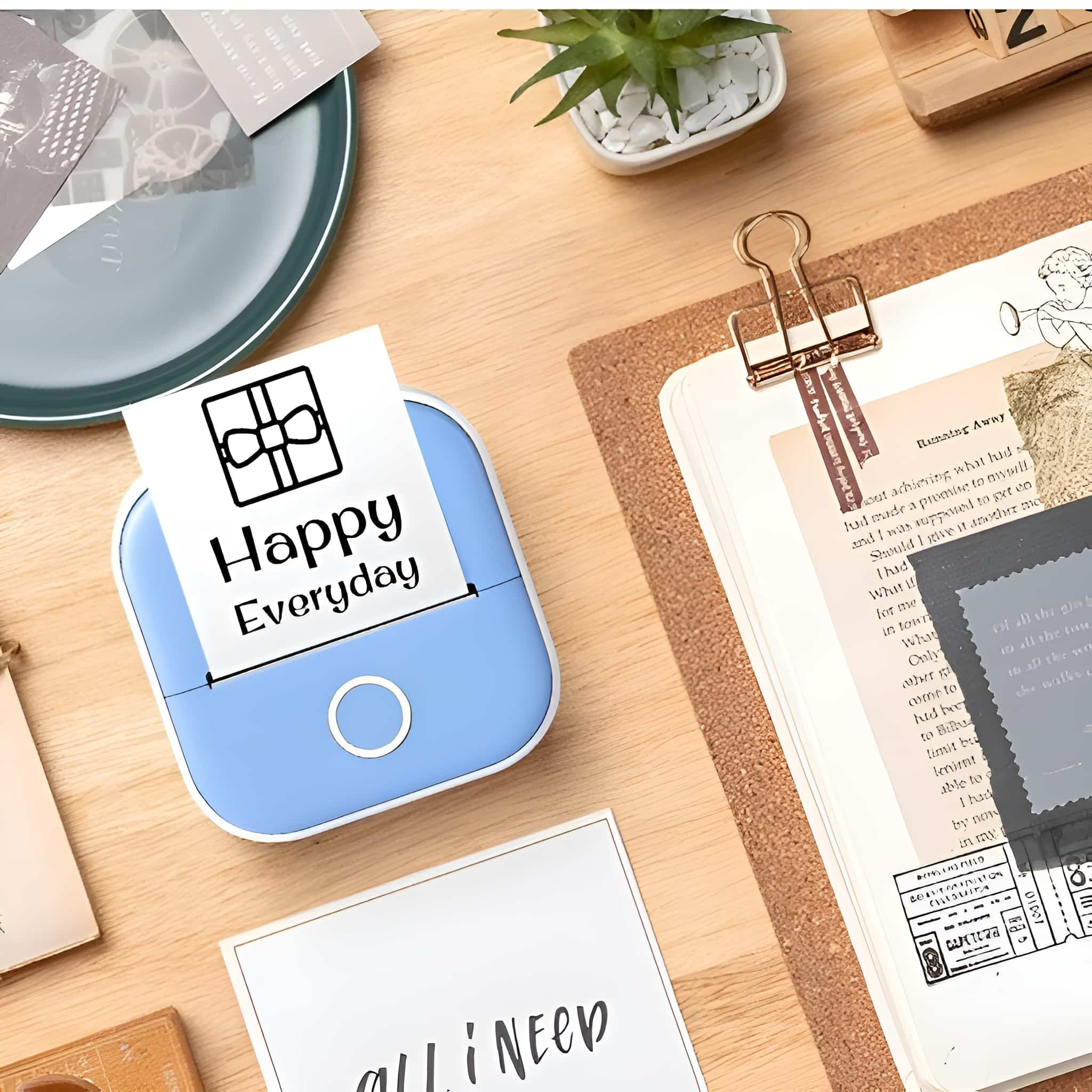 Ein blauer Mini-Drucker auf einem Schreibtisch druckt Papier mit der Aufschrift Happy Everyday.
