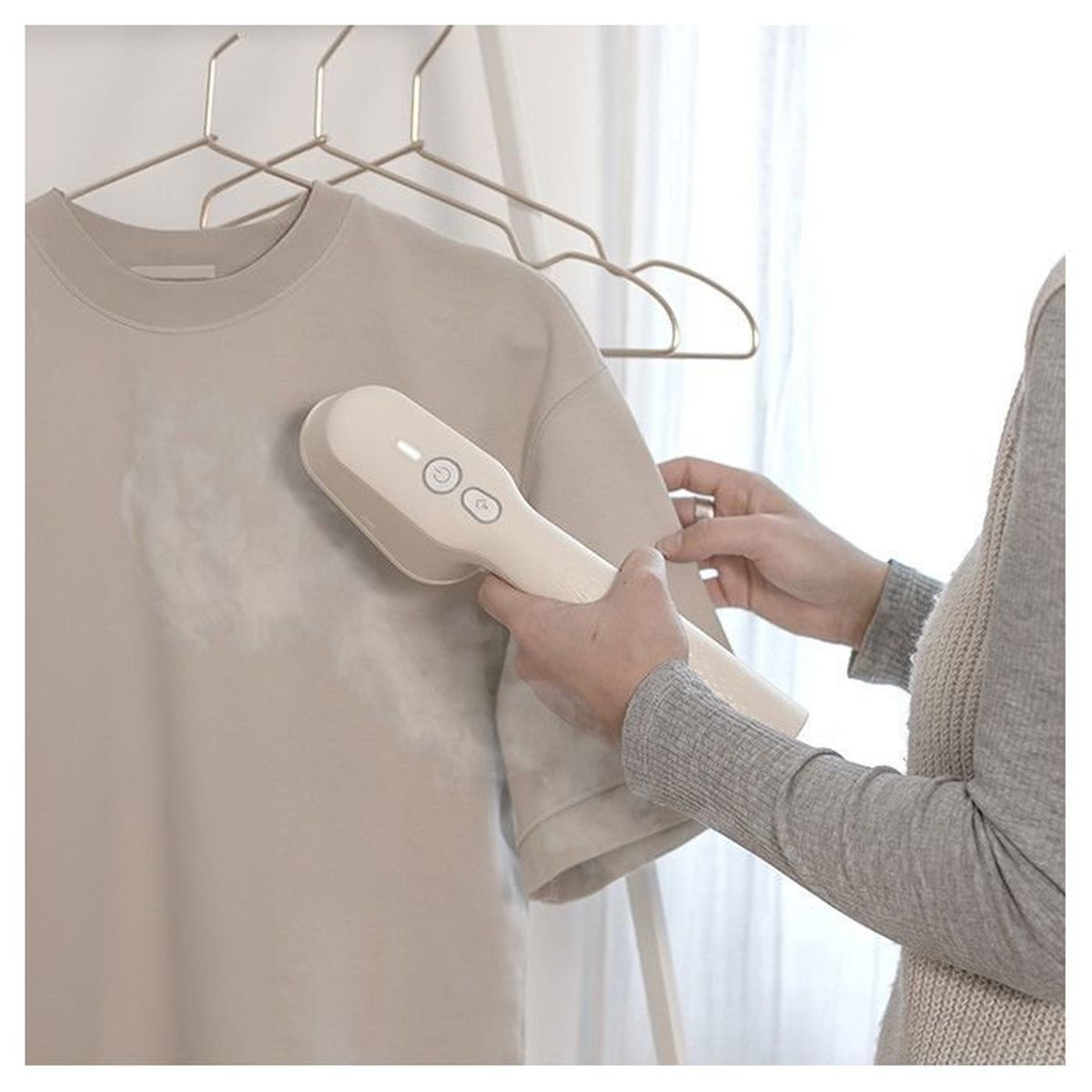 Eine Person bügelt ein beiges T-Shirt an einem Kleiderbügel mit einem Handdampfgarer.
