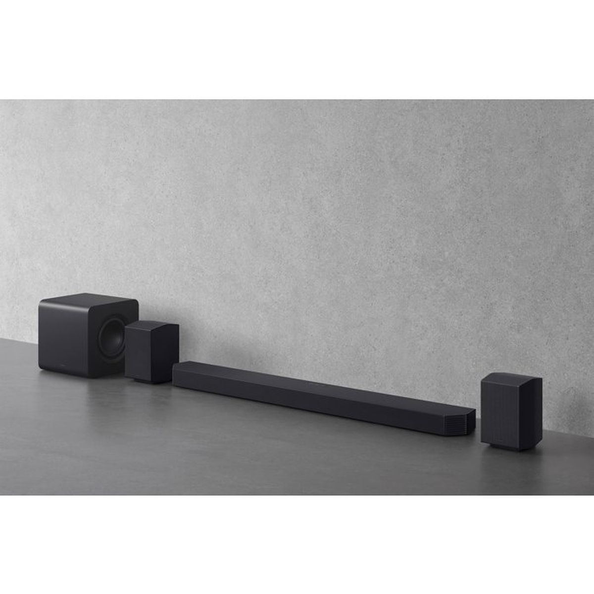 Ein schwarzes Soundbar-System mit Subwoofer und Lautsprechern auf einer dunklen Oberfläche vor einer grauen Wand.