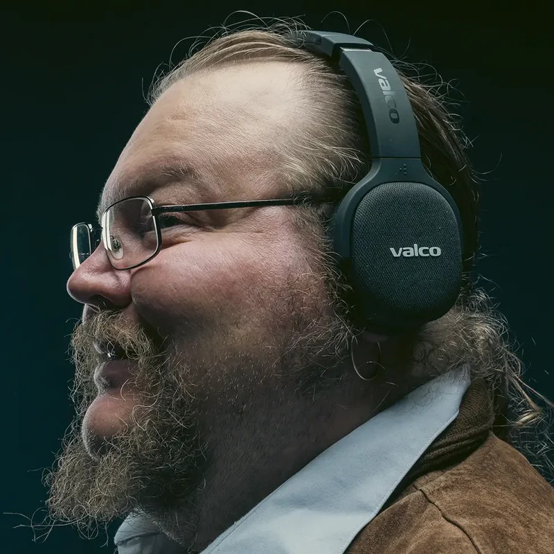 Ein Mann mit Brille und Valco-Kopfhörern im Profil vor dunklem Hintergrund.