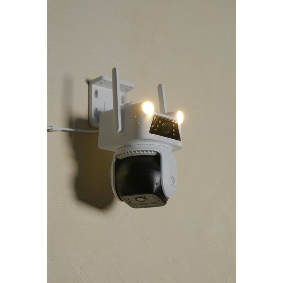 Eine weiße Überwachungskamera mit zwei Antennen und beleuchteten Flutlichtern an einer Wand.