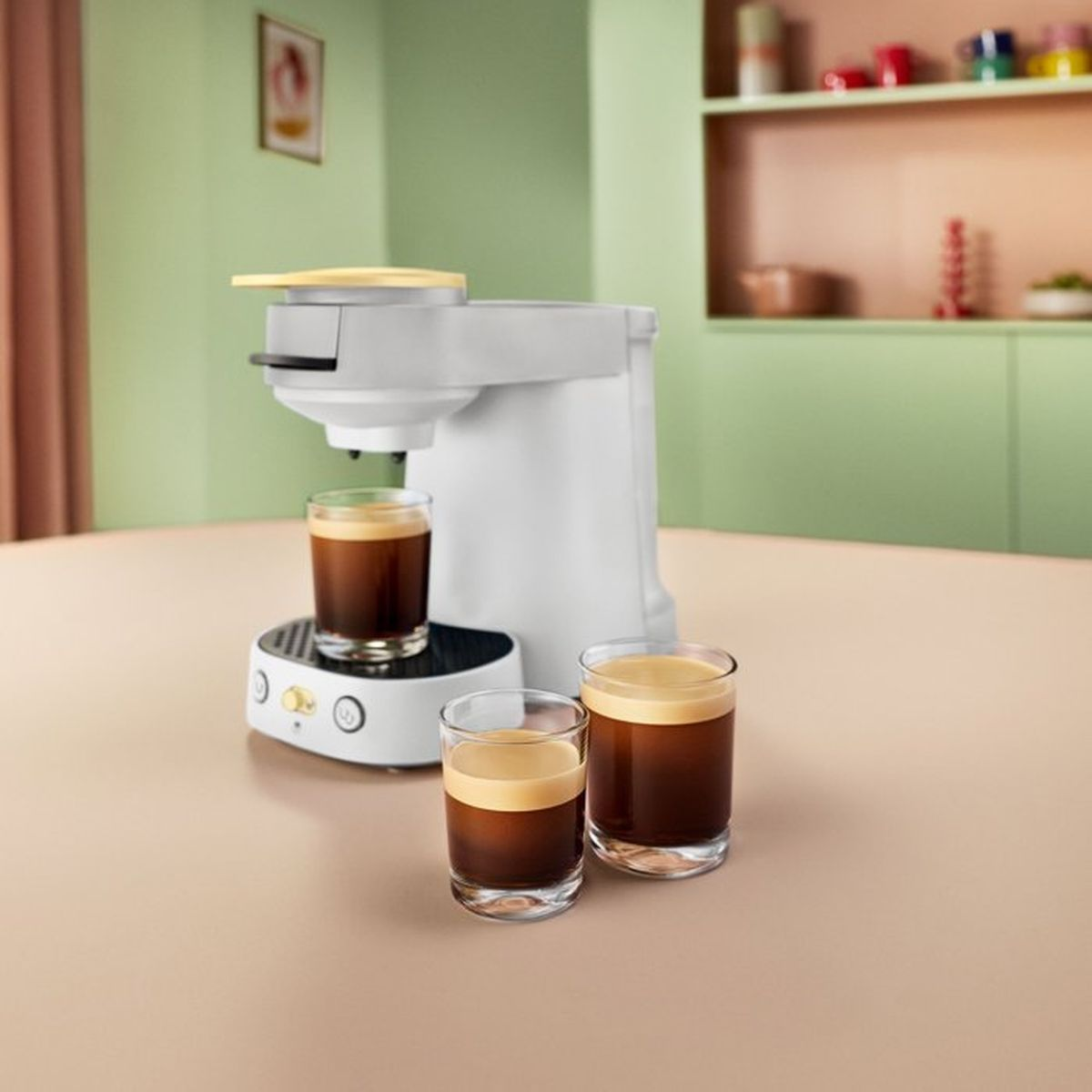 Eine weiße Kaffeemaschine auf einem Tisch mit drei Gläsern Kaffee.