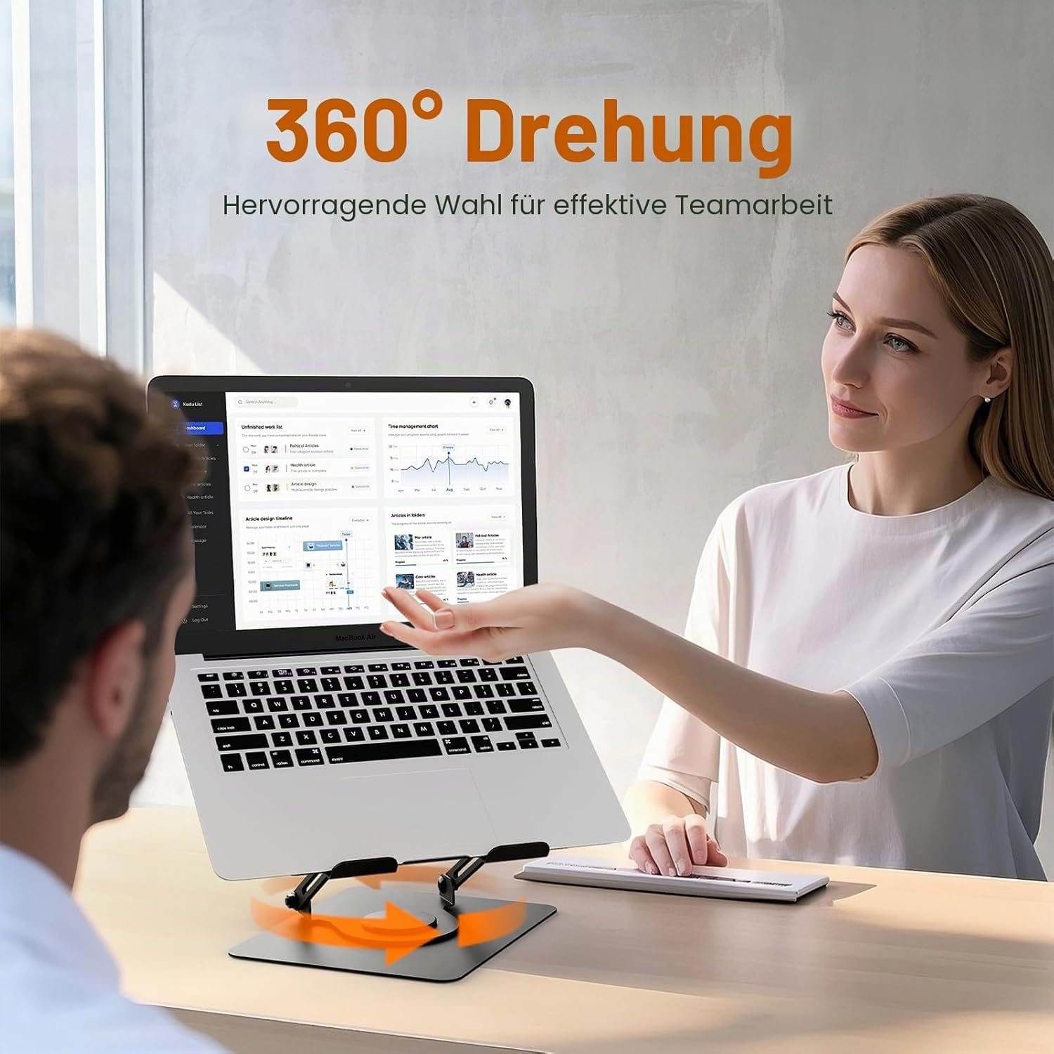 Zwei Personen nutzen einen Laptop auf einem drehbaren Ständer an einem Holztisch.