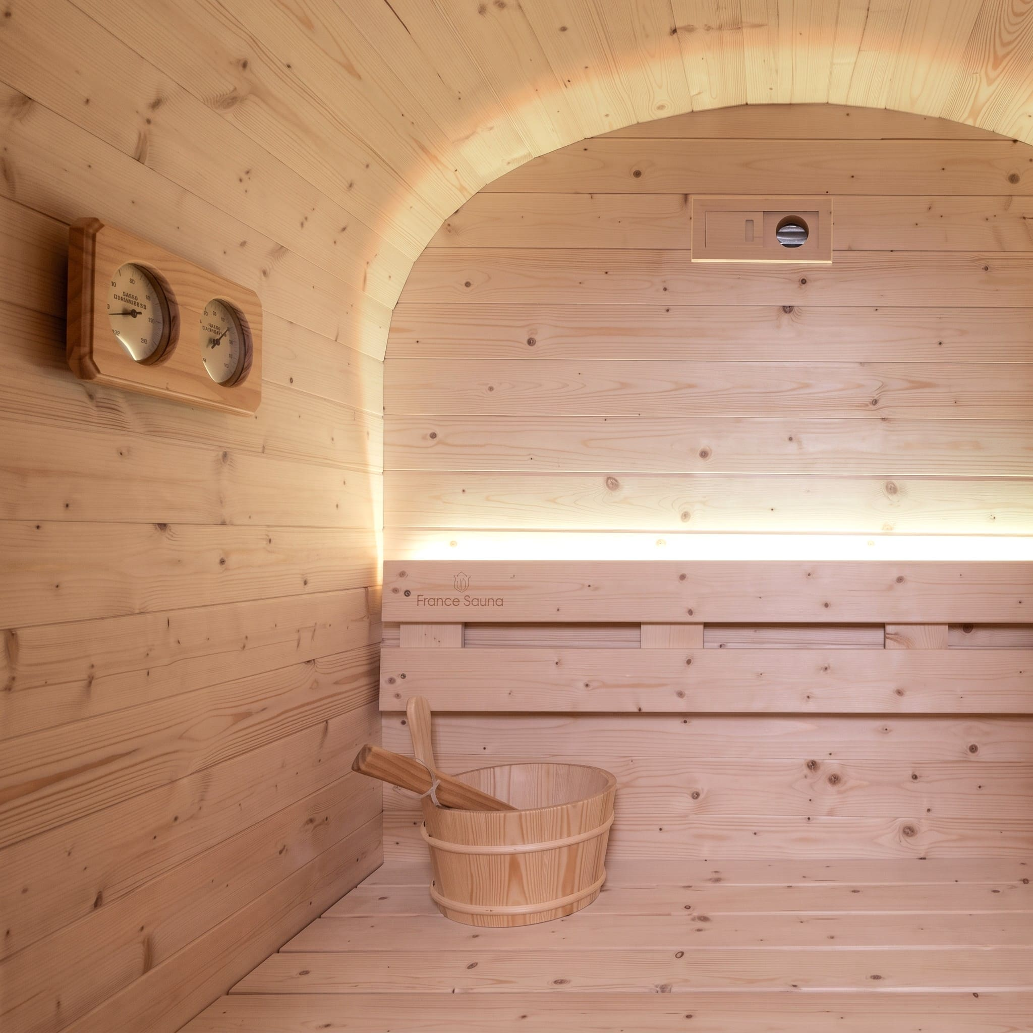 Interior de sauna de madera con termohigrómetro, banco, iluminación LED, cubo y cucharón.