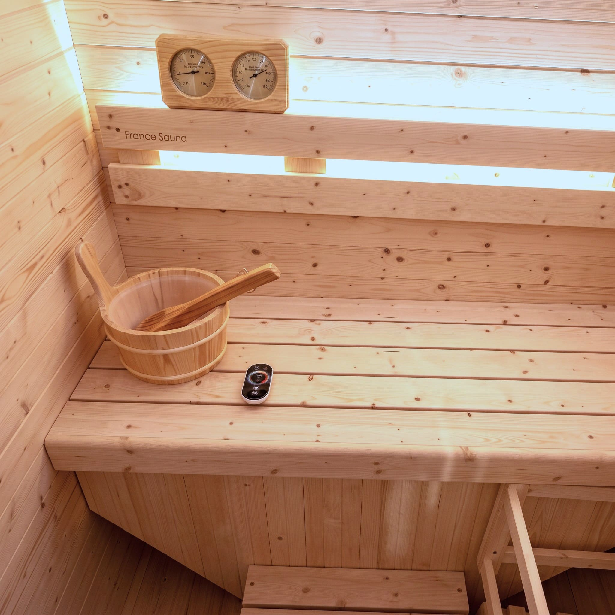 Interior de sauna de madera con cubo, cucharón, panel de control y termómetro.