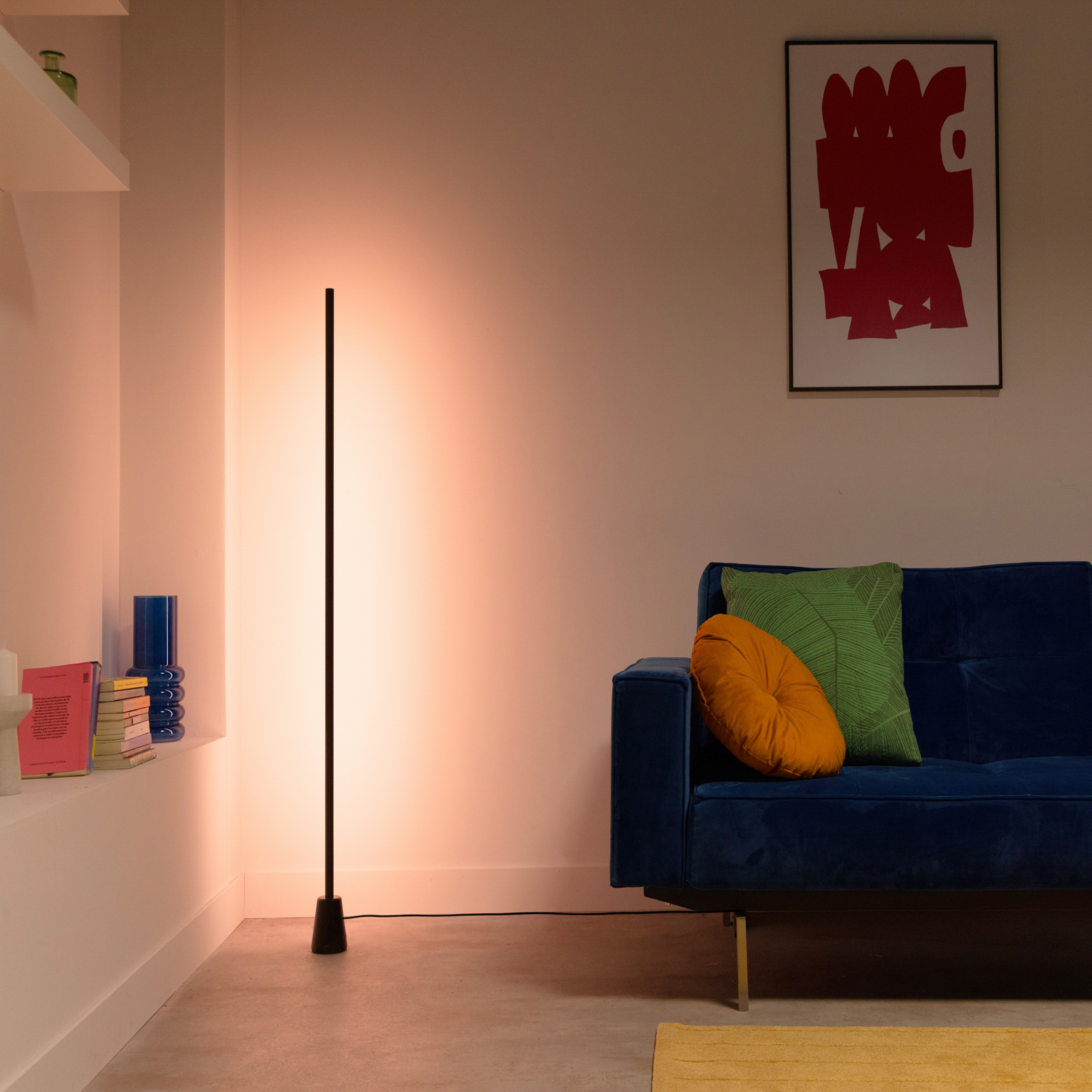 Mavi kanepe, renkli yastıklar, minimalist lambader ve soyut sanat eseri içeren şık bir oturma odası.