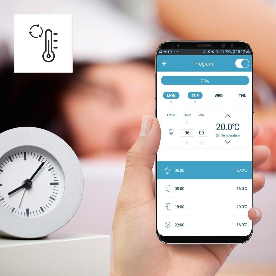 Eine Hand hält ein Smartphone mit einer Thermostat-App, neben einem silbernen Wecker mit weißem Zifferblatt.
