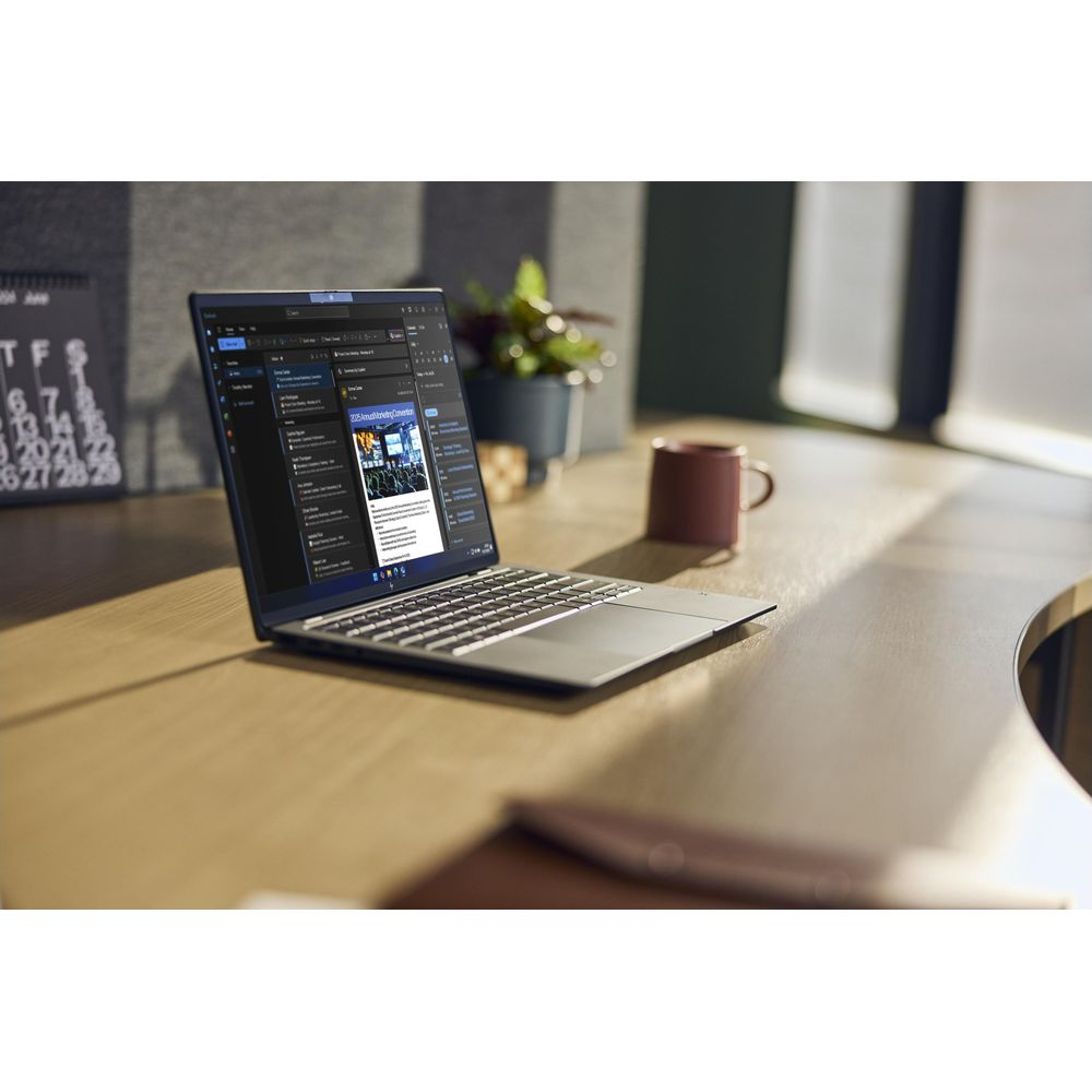 Un computer portatile su una scrivania di legno in un ufficio soleggiato, con tazza e pianta sullo sfondo.