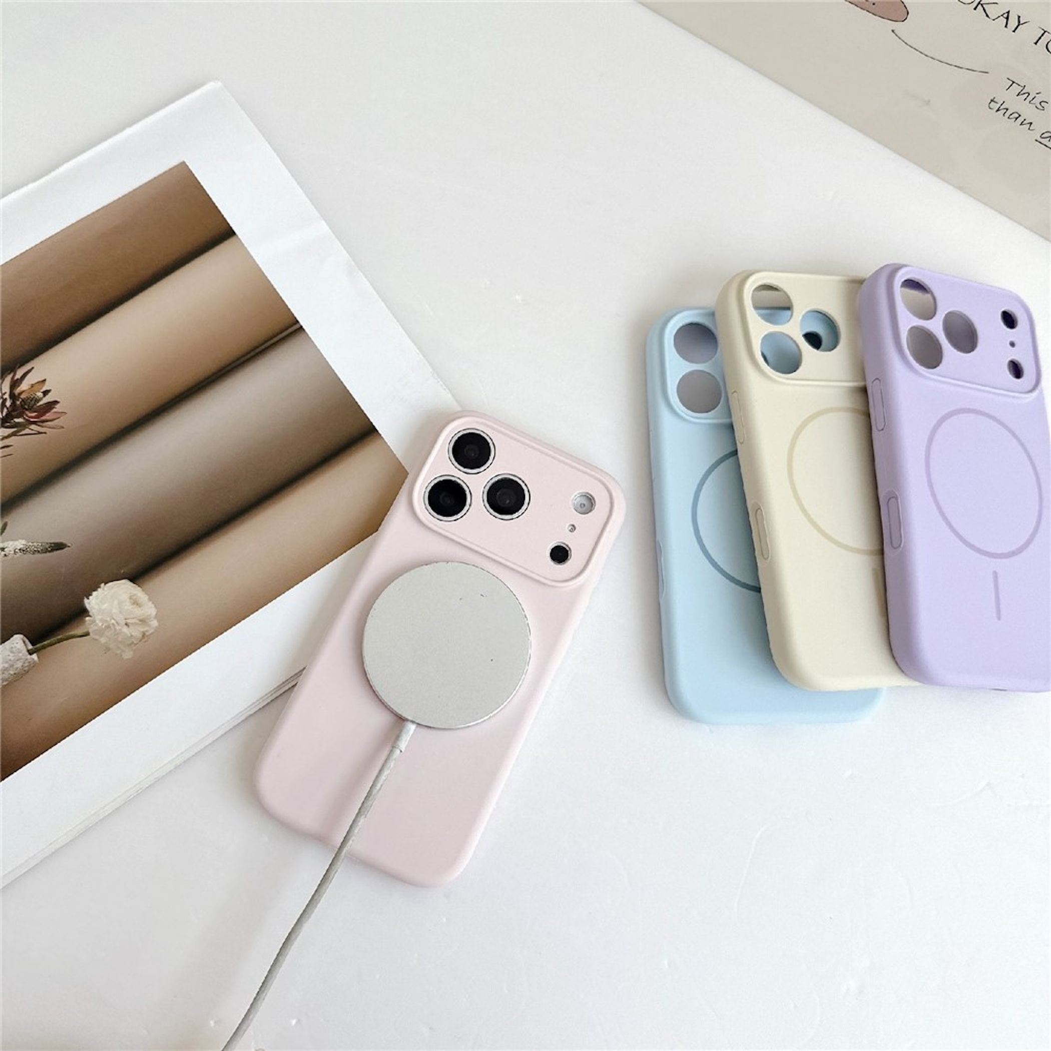 Pastellfarbene Smartphone-Hüllen und ein pinkes Handy mit Ladekabel auf weißem Tisch.