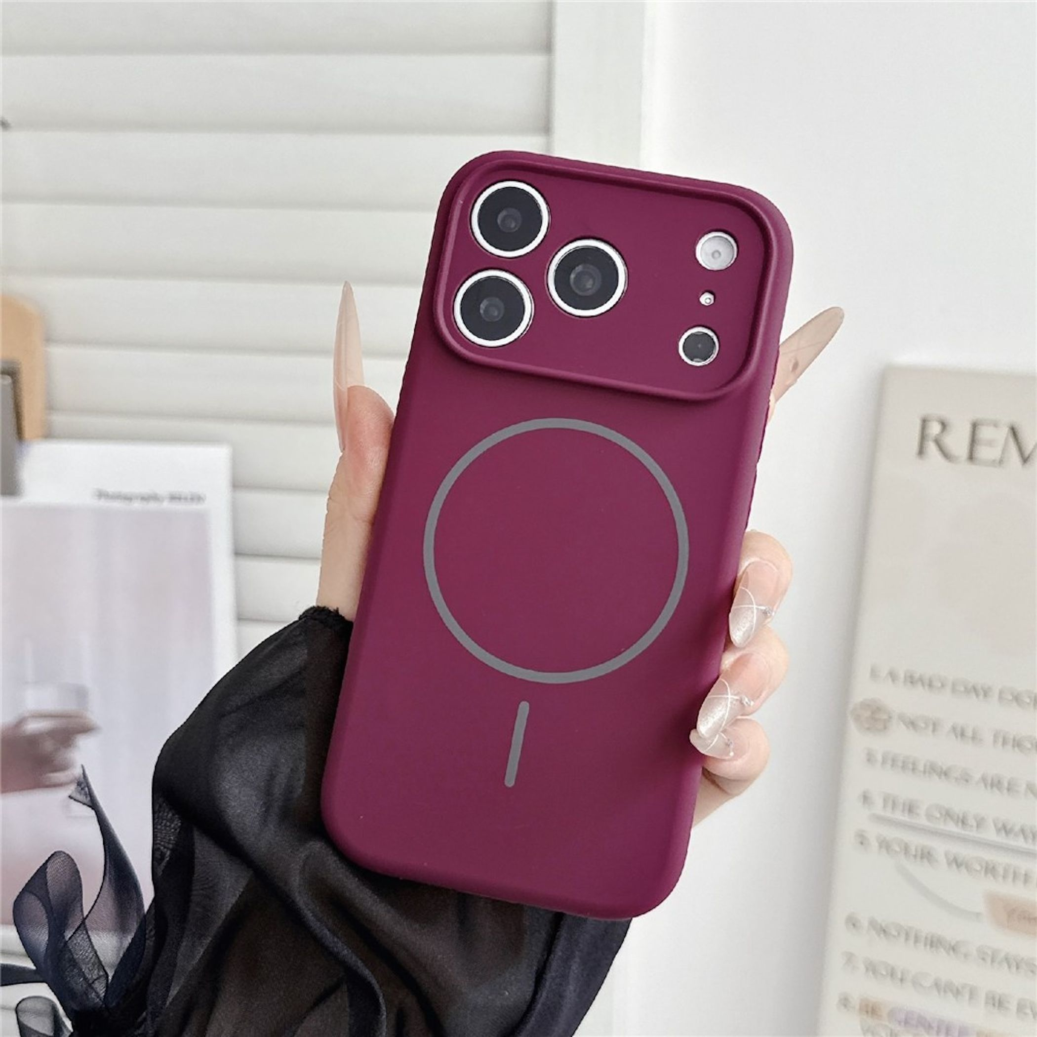 Eine Hand hält eine dunkellila Smartphone-Hülle mit kreisförmigem MagSafe-Symbol und Kameraschutz.