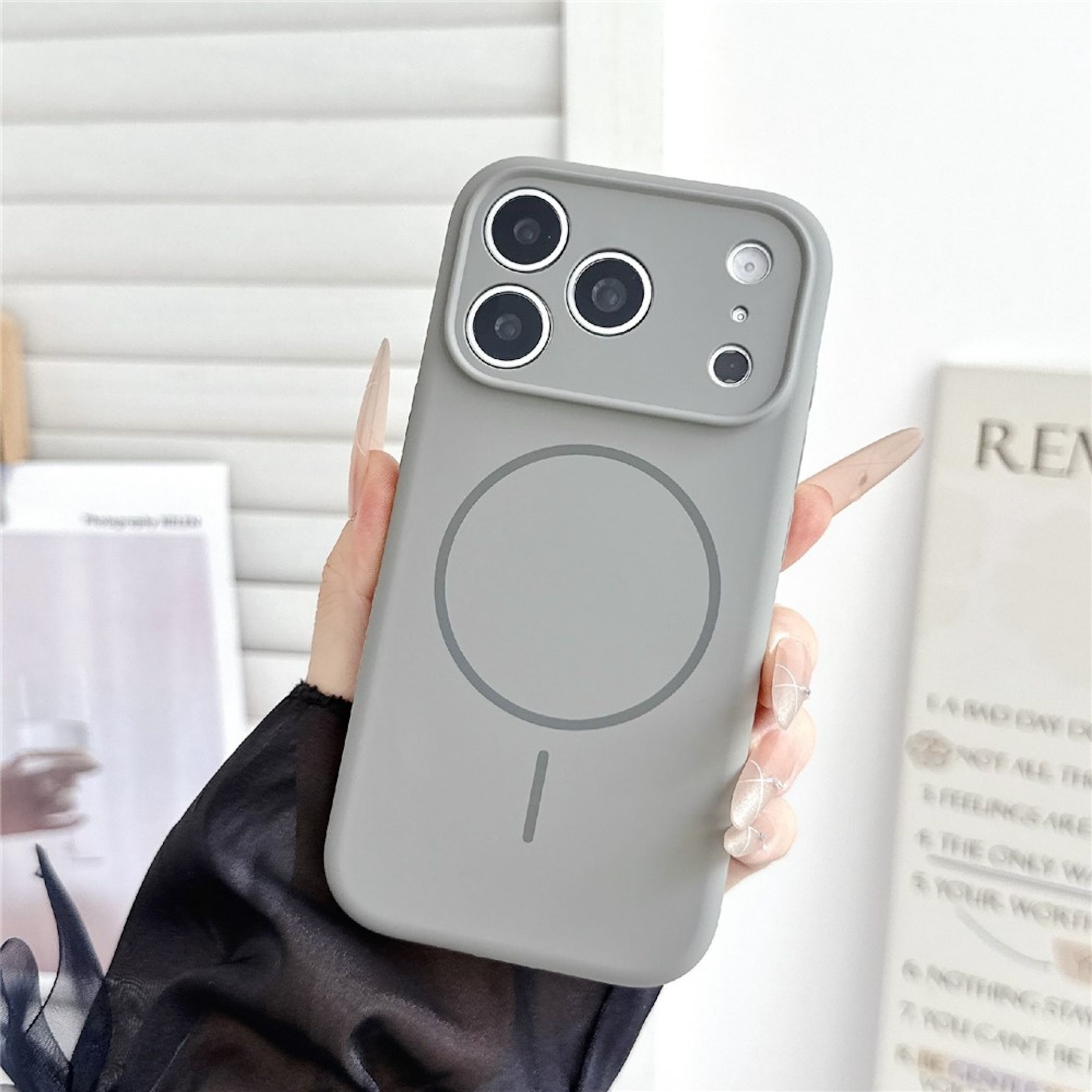 Hand mit langen Nägeln hält ein graues Smartphone mit Kameraausschnitt und runder Markierung.