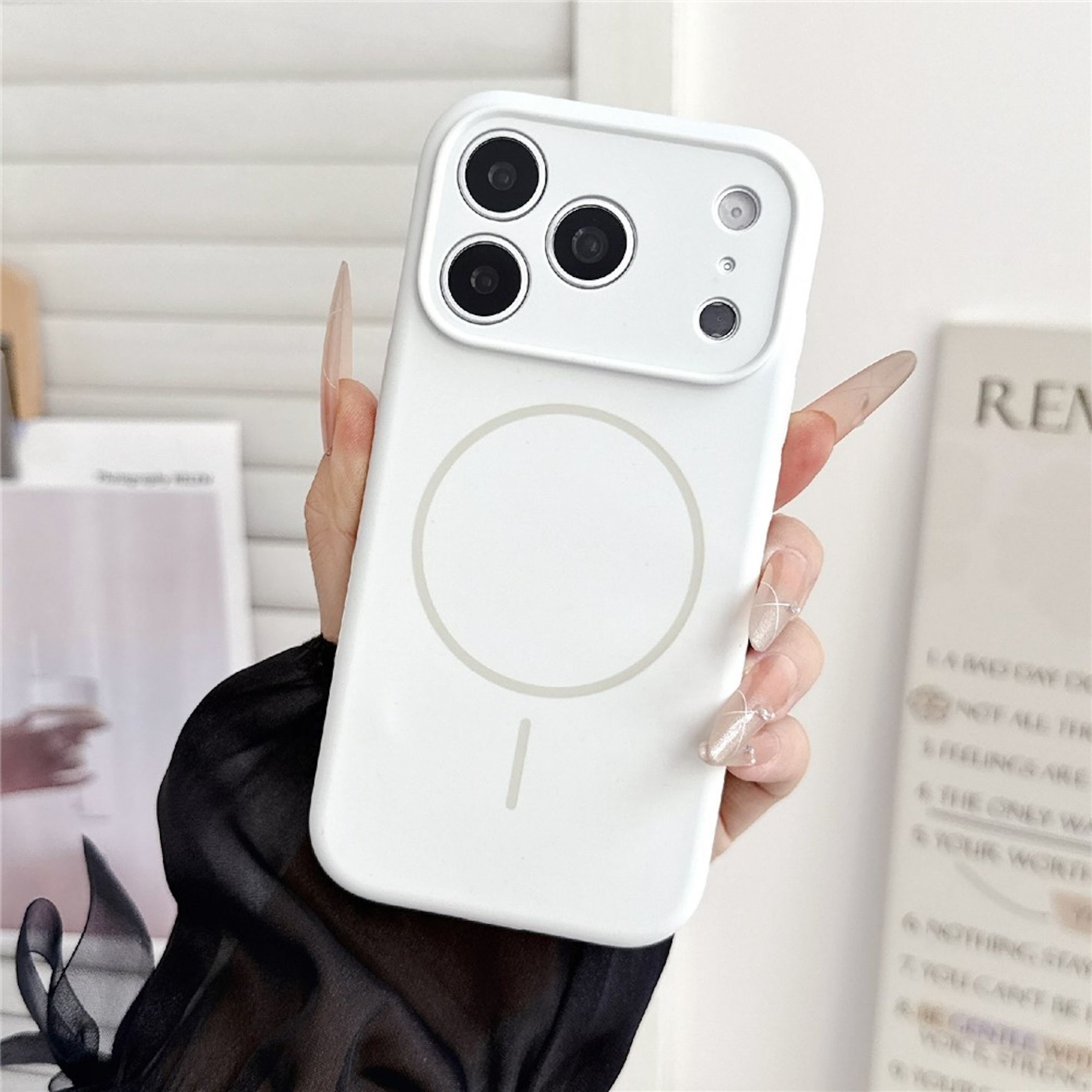 Hand mit langen, verzierten Nägeln hält eine weiße Smartphone-Hülle mit MagSafe-Ring.