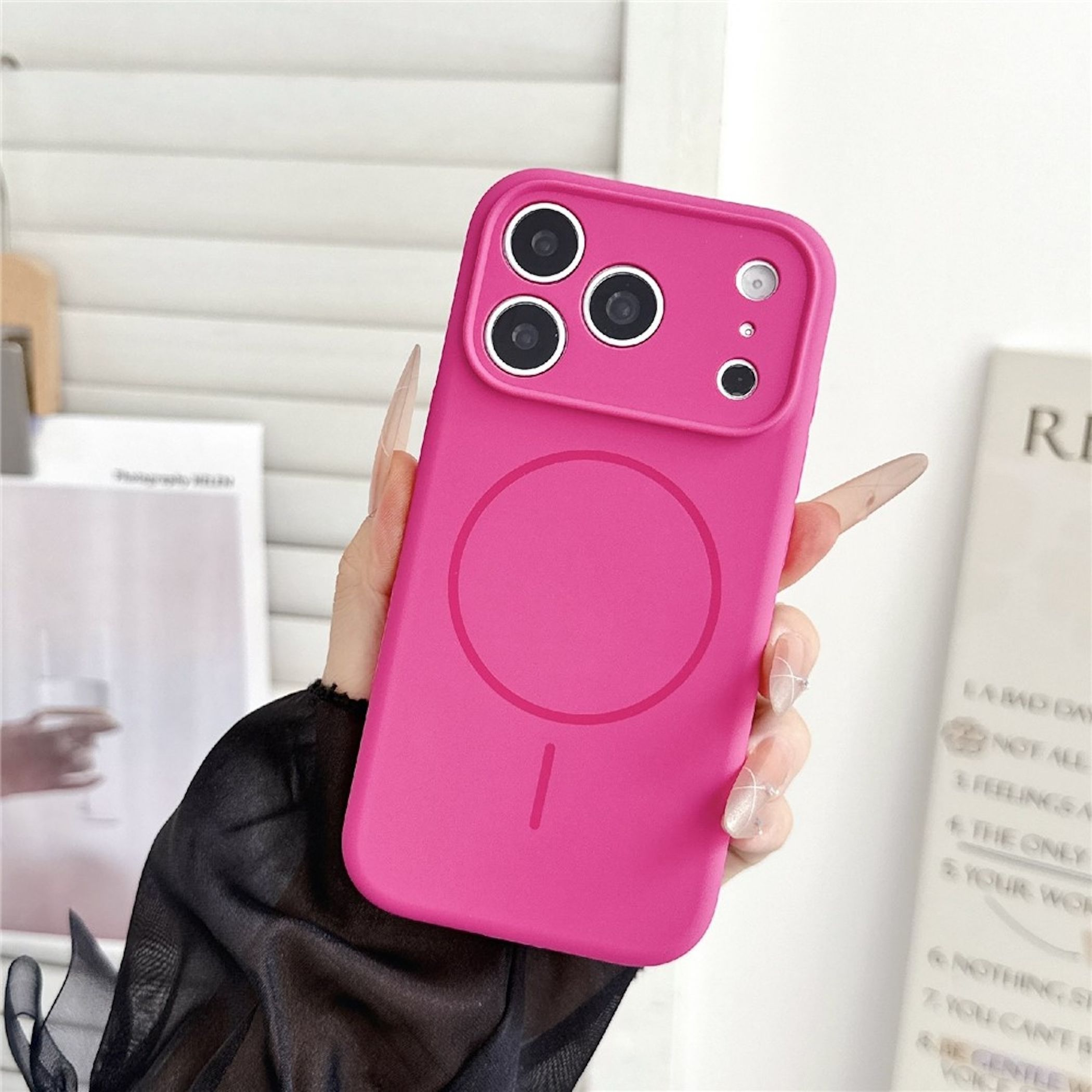 Eine Hand hält eine pinkfarbene Smartphone-Hülle mit Kameraausschnitt und MagSafe-Ring.